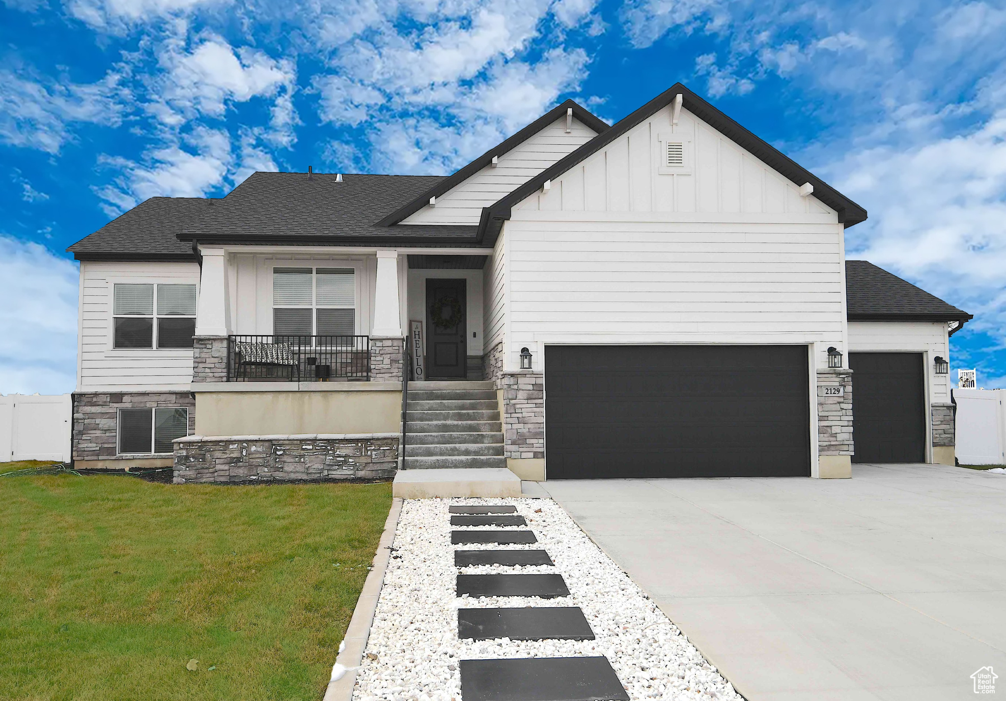 View of front of home featuring a front yard, concrete driveway, a garage, stone siding, and board and batten siding