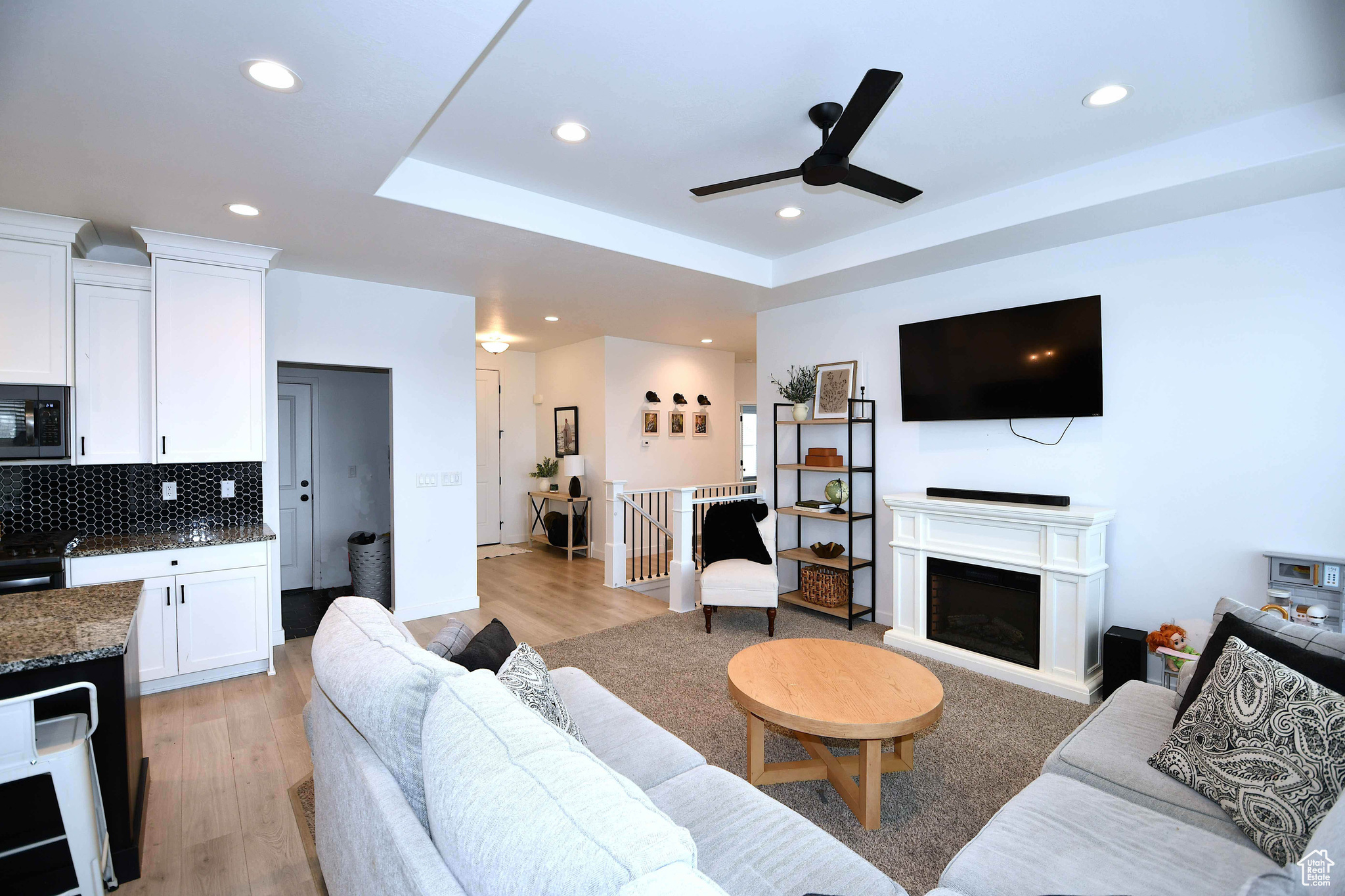Living room with light hardwood / wood-style flooring, a raised ceiling, and ceiling fan
