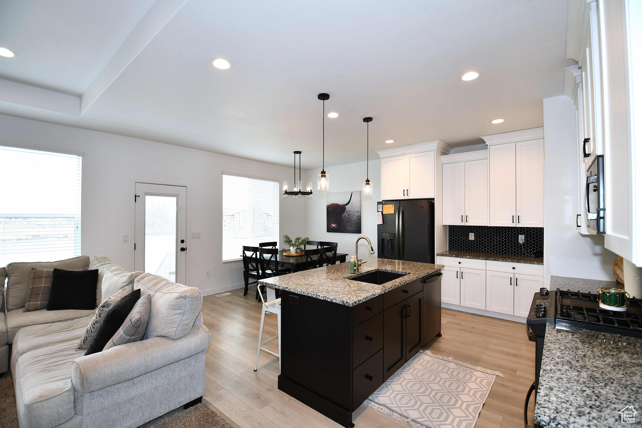 Kitchen with black appliances, white cabinets, sink, light hardwood / wood-style flooring, and an island with sink
