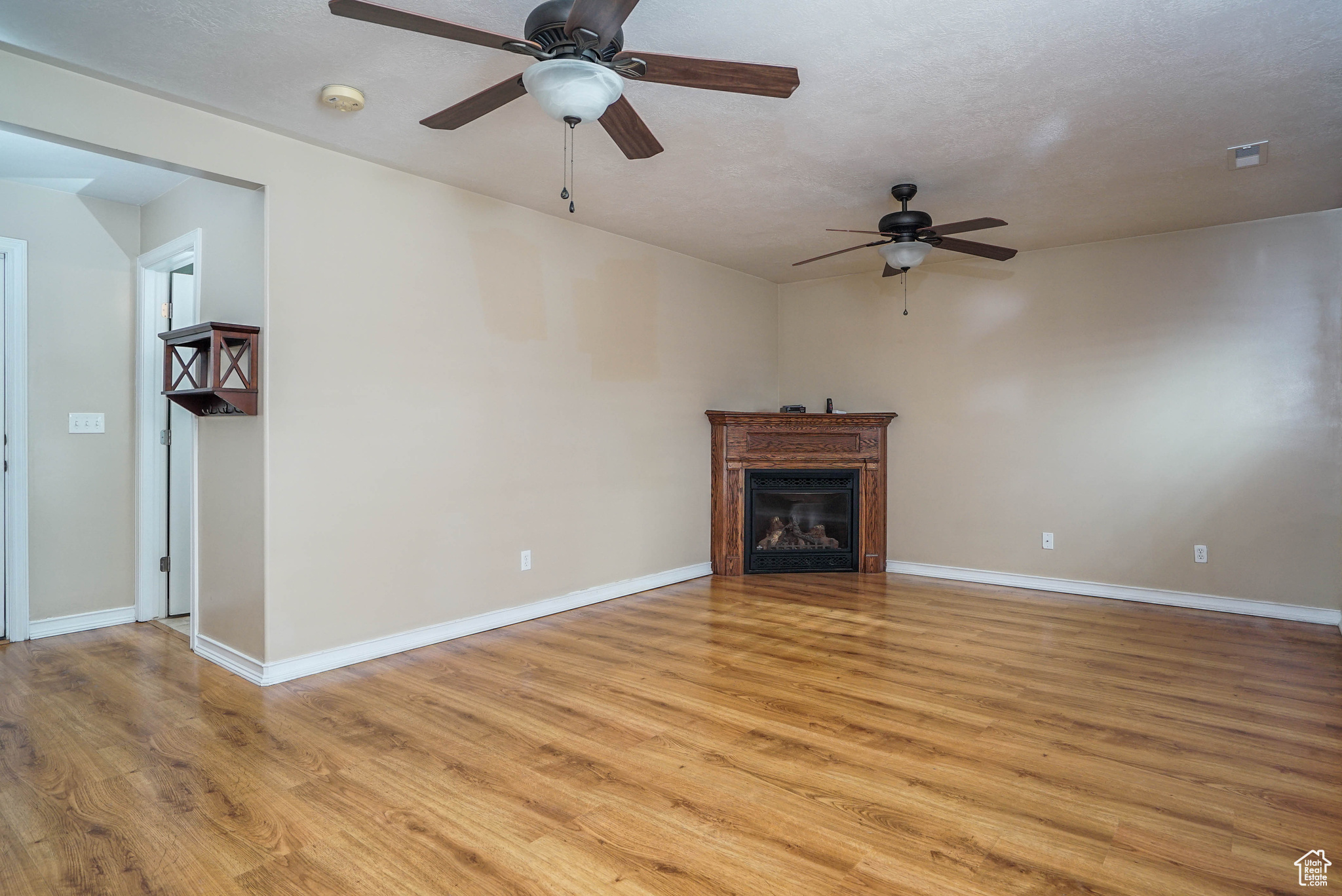 Unfurnished living room featuring ceiling fan, a textured ceiling, and light wood-type flooring