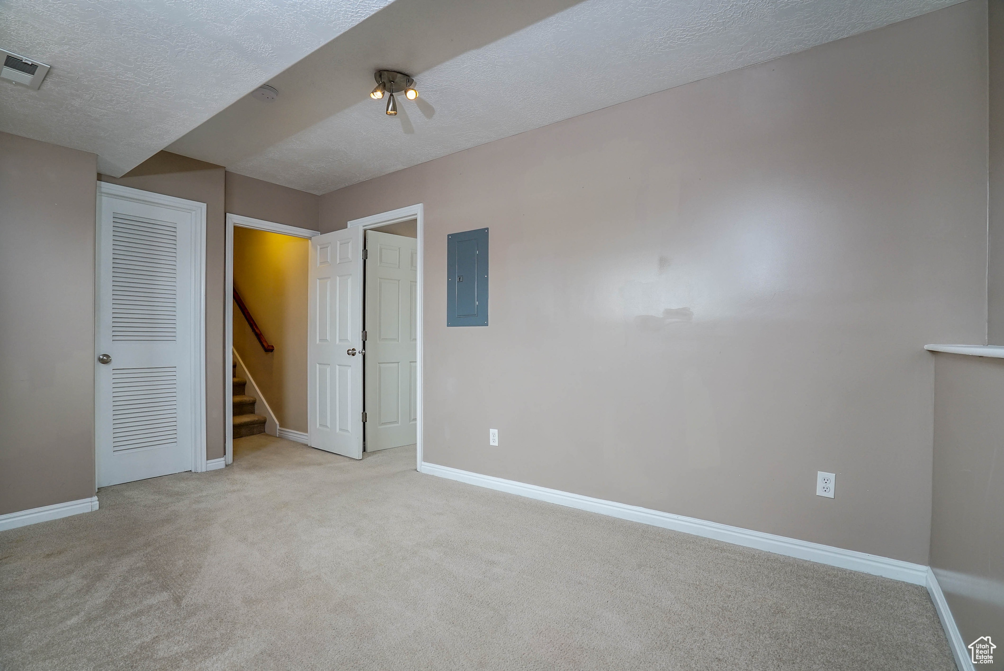 Unfurnished bedroom featuring a textured ceiling, electric panel, and light colored carpet