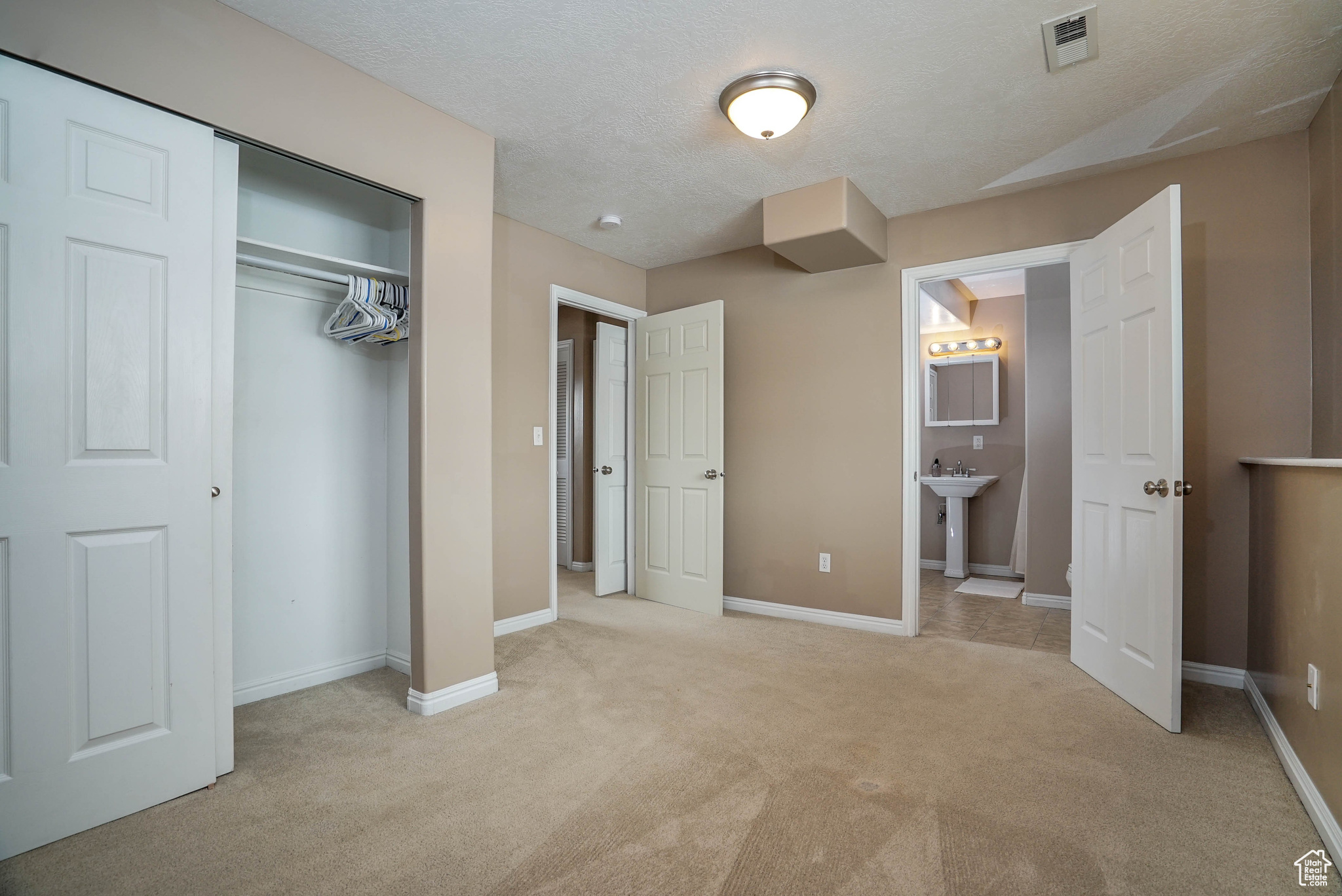 Unfurnished bedroom with sink, ensuite bath, a textured ceiling, light colored carpet, and a closet