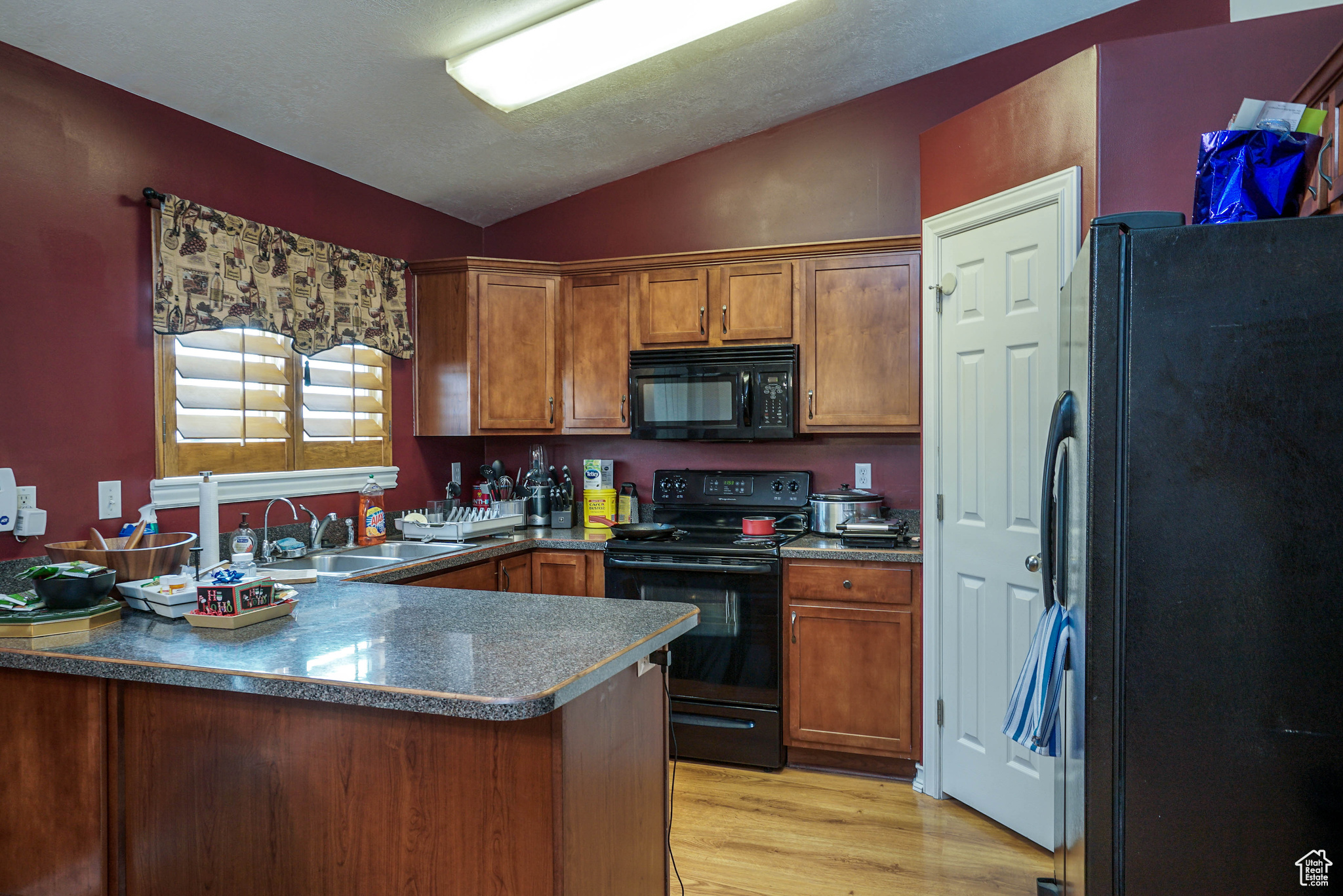 Kitchen featuring sink, kitchen peninsula, vaulted ceiling, black appliances, and light wood-type flooring