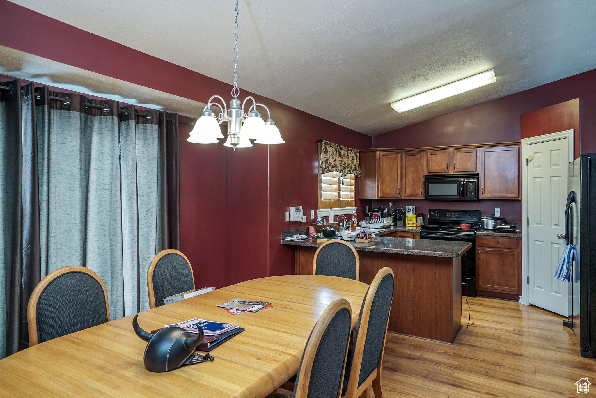 Kitchen featuring hanging light fixtures, light hardwood / wood-style flooring, a notable chandelier, lofted ceiling, and black appliances