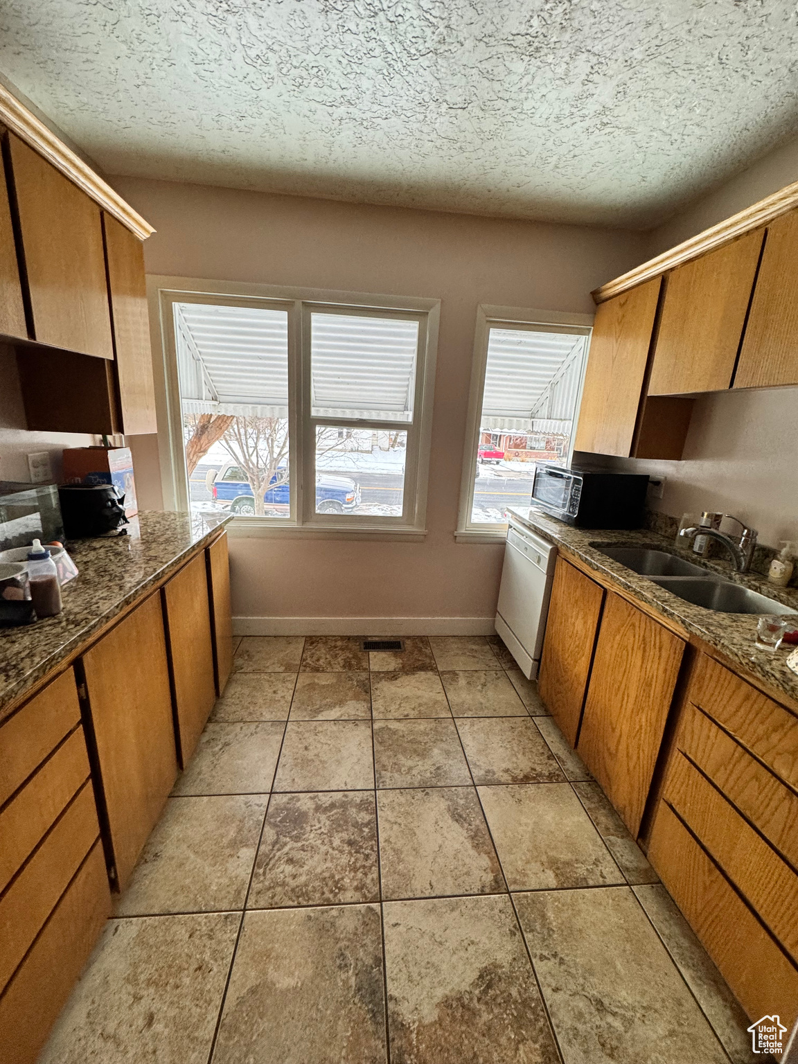 Kitchen featuring light tile patterned floors, a textured ceiling, white dishwasher, a sink, and brown cabinets