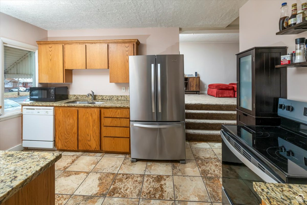 Kitchen featuring light stone countertops, a textured ceiling, stainless steel appliances, and sink