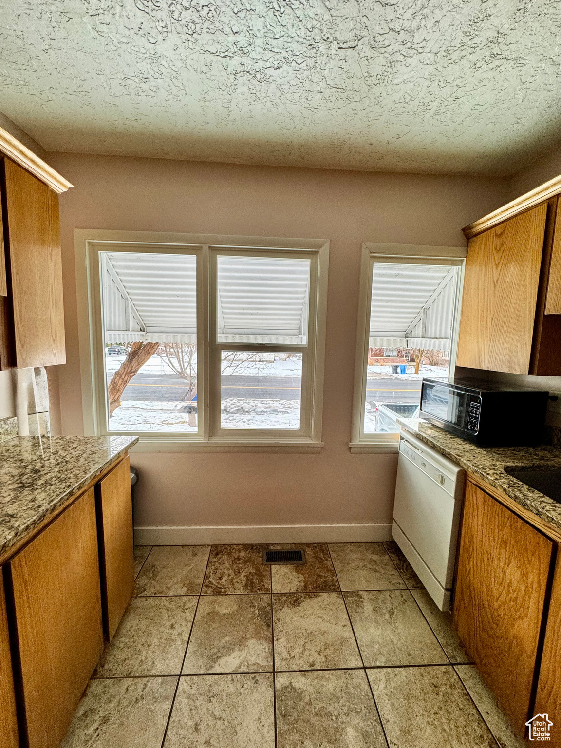 Kitchen with black microwave, white dishwasher, visible vents, baseboards, and brown cabinets