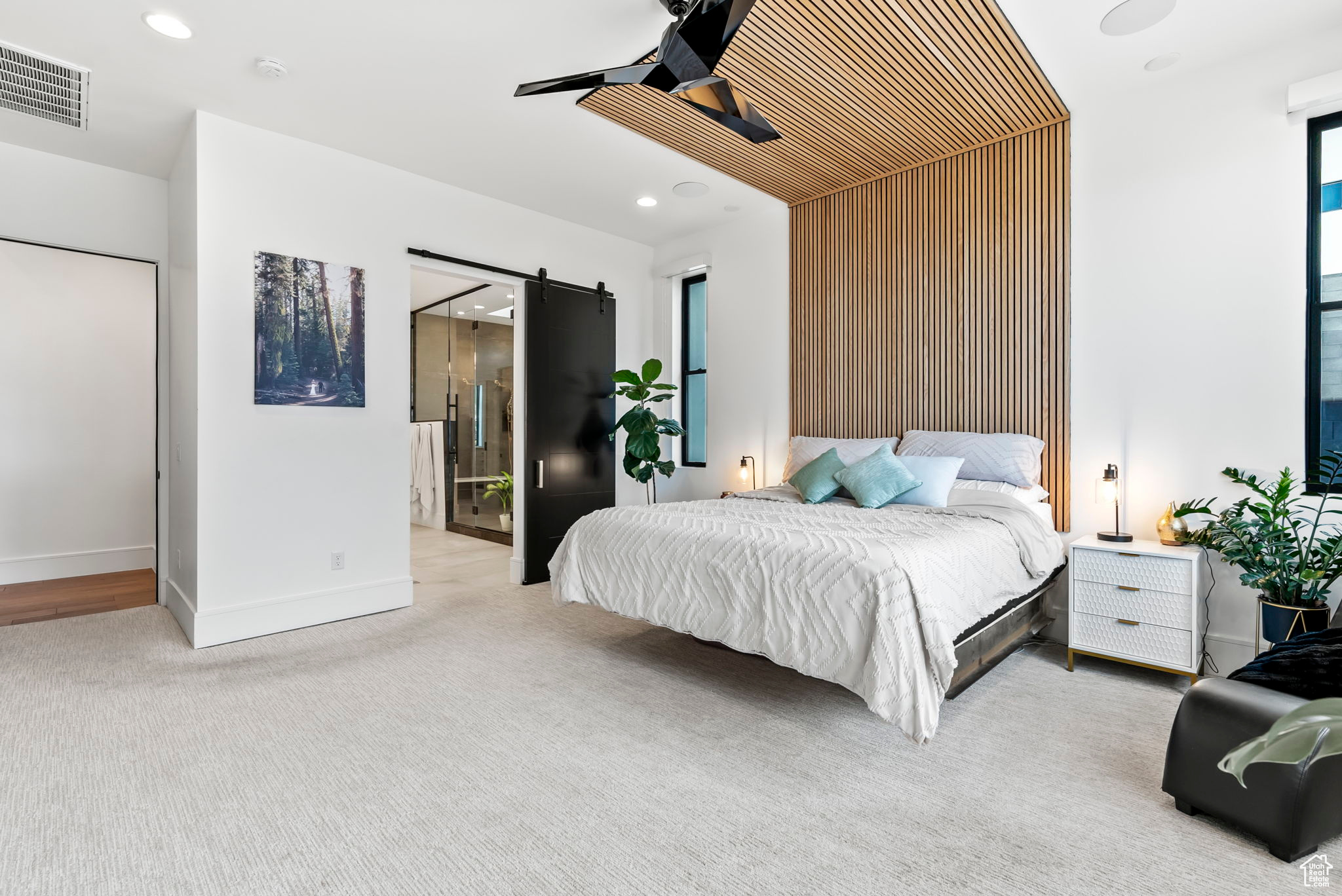 Carpeted bedroom featuring ceiling fan, a barn door, wooden walls, and ensuite bath