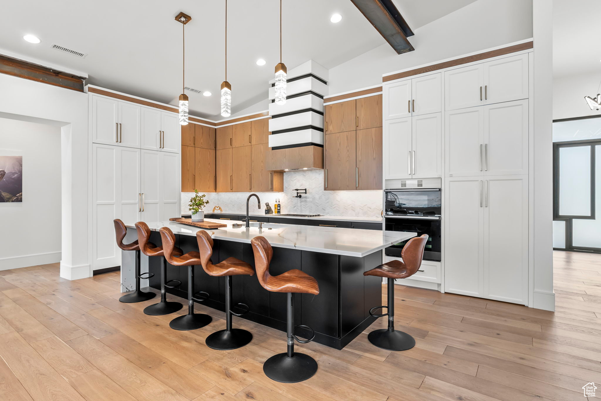 Kitchen featuring decorative backsplash, a breakfast bar, decorative light fixtures, a center island with sink, and white cabinets