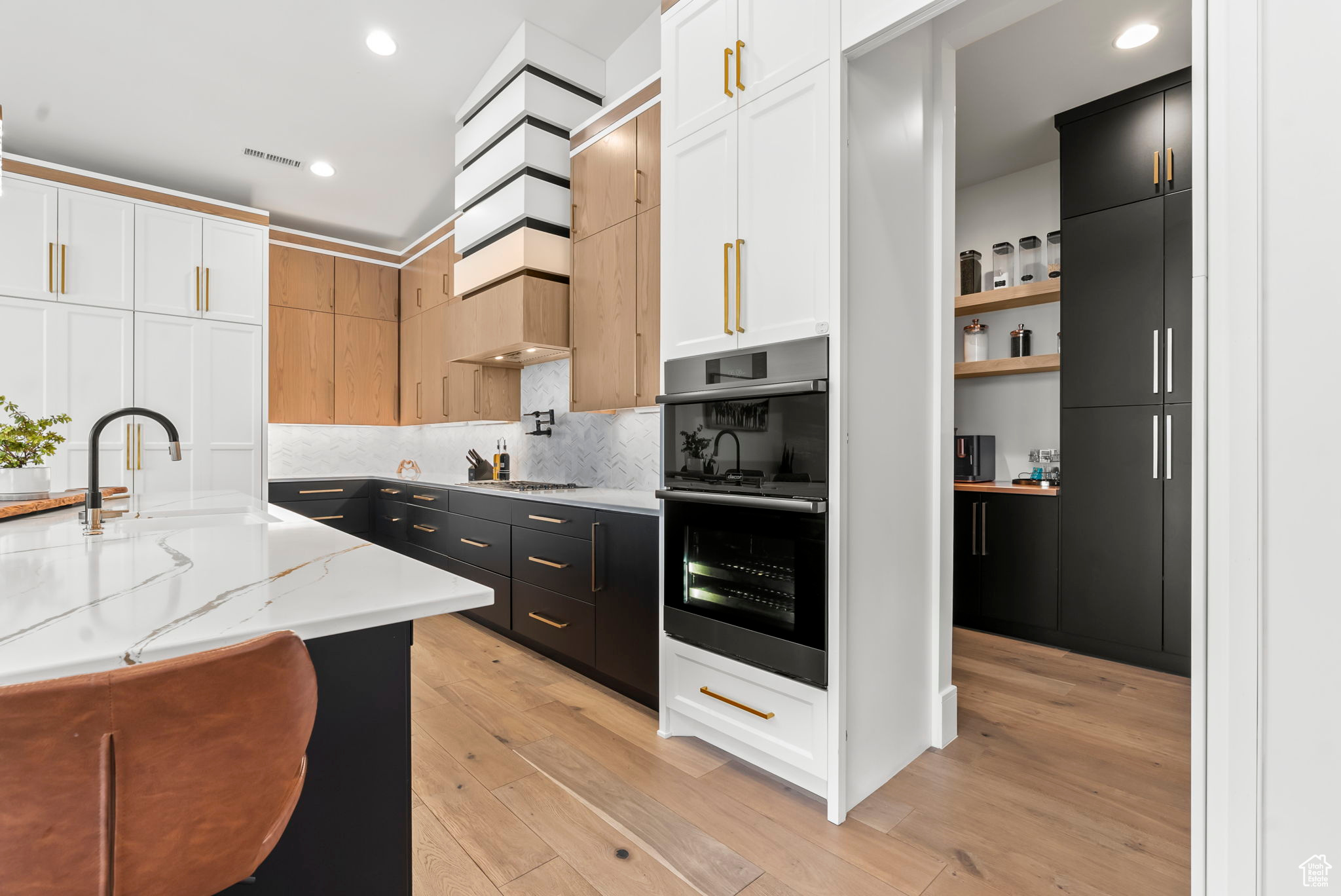 Kitchen featuring light stone counters, white cabinetry, double oven, and light hardwood / wood-style flooring