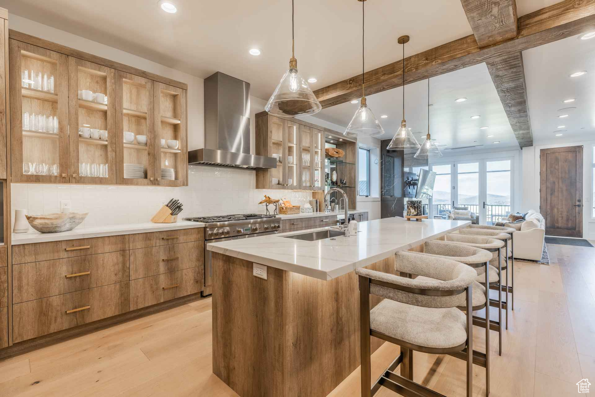 Kitchen featuring a breakfast bar, a large island with sink, wall chimney range hood, sink, and light hardwood / wood-style floors