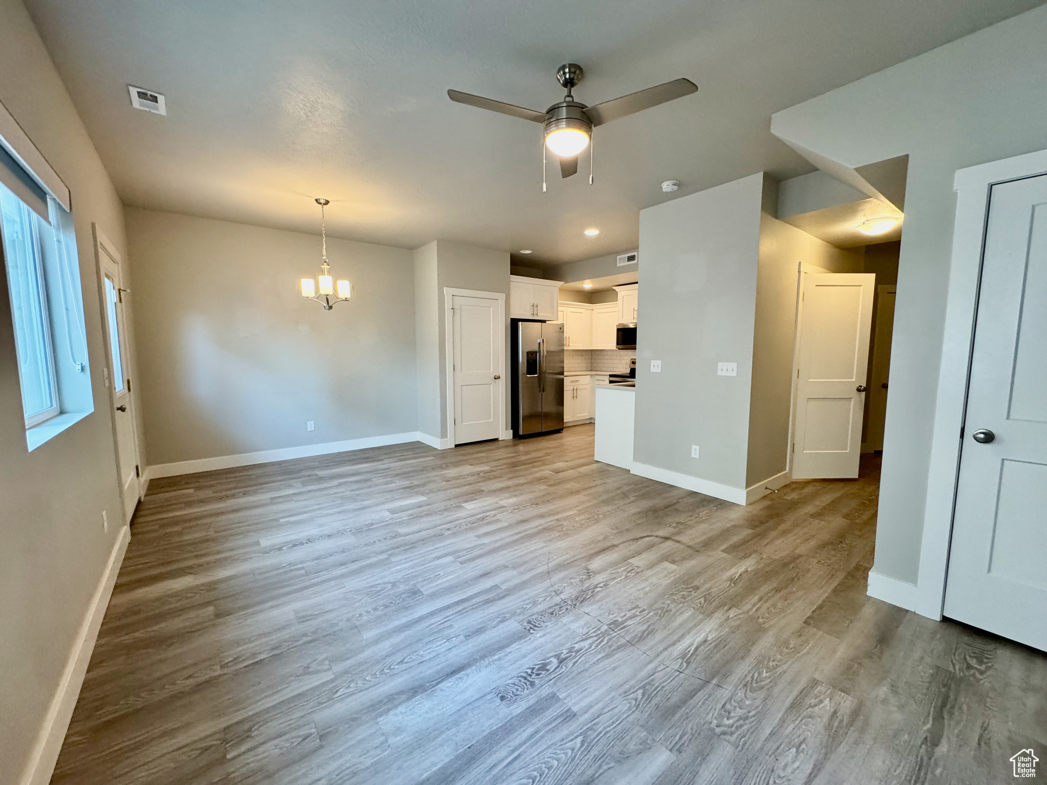 Unfurnished living room featuring ceiling fan with notable chandelier and light hardwood / wood-style flooring