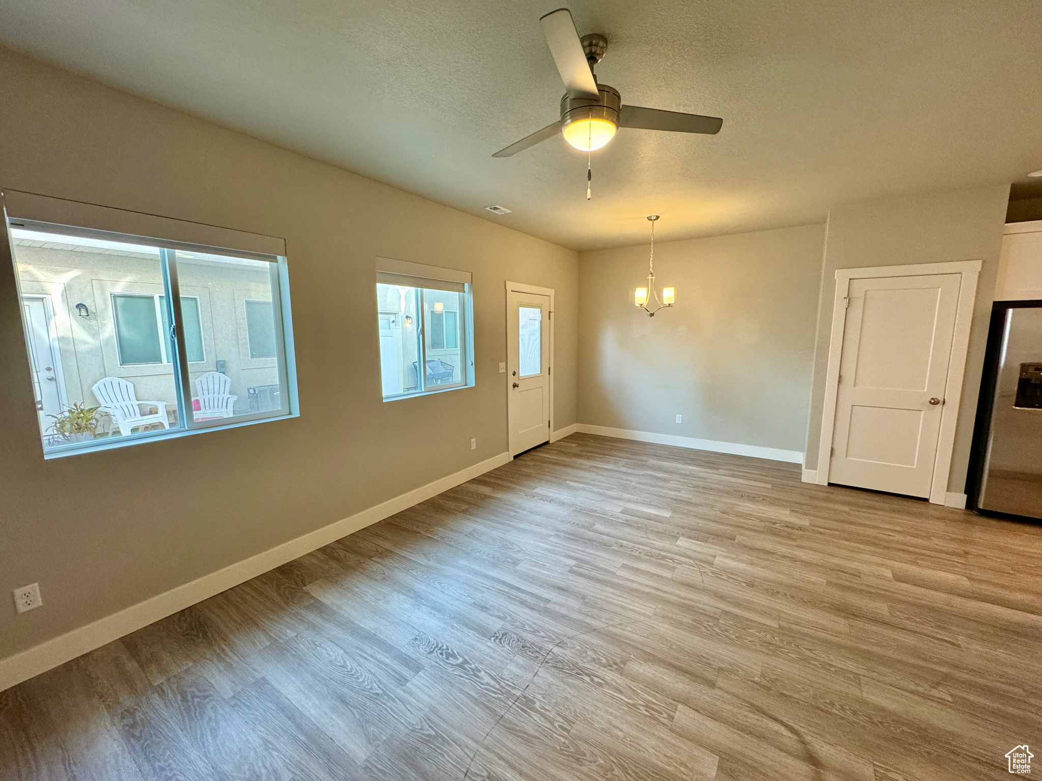 Spare room with ceiling fan with notable chandelier, a textured ceiling, and light wood-type flooring