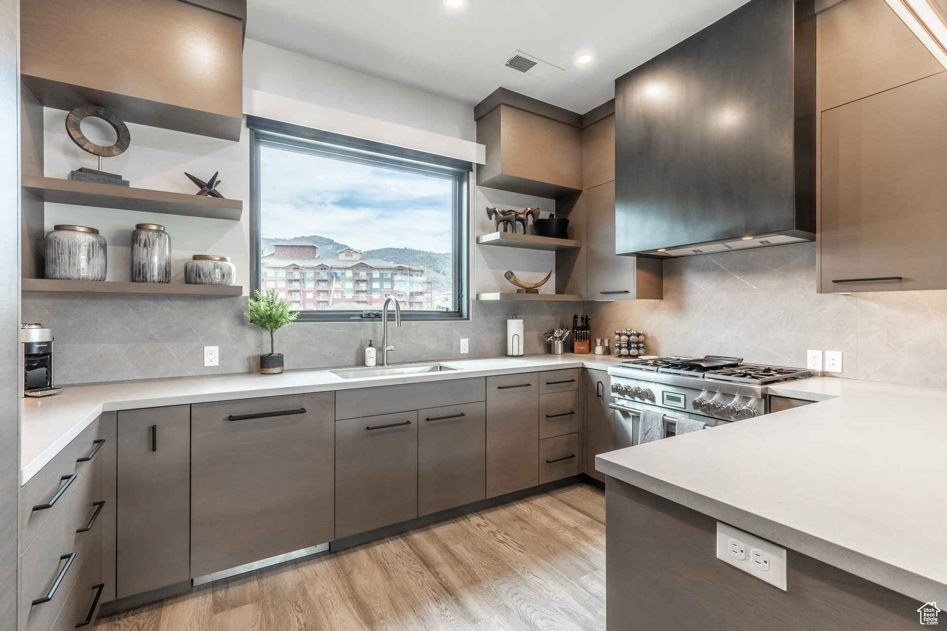 Kitchen with wall chimney range hood, sink, stainless steel stove, decorative backsplash, and light wood-type flooring