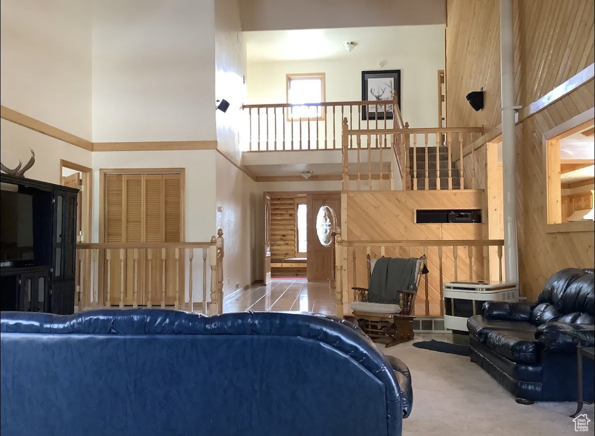 Living room featuring a towering ceiling, tile patterned floors, and wood walls