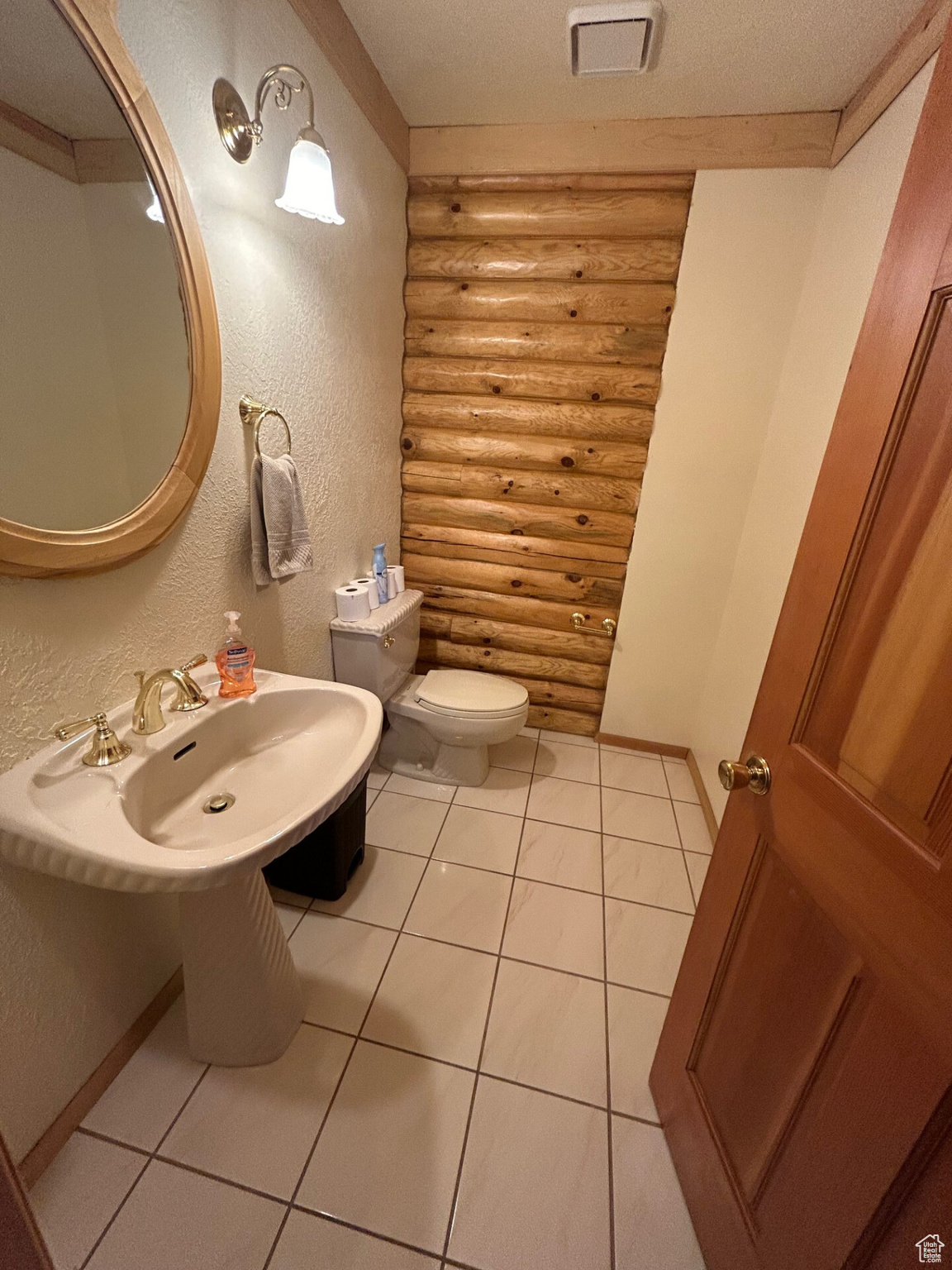 Bathroom with tile patterned flooring, toilet, ornamental molding, rustic walls, and a textured ceiling