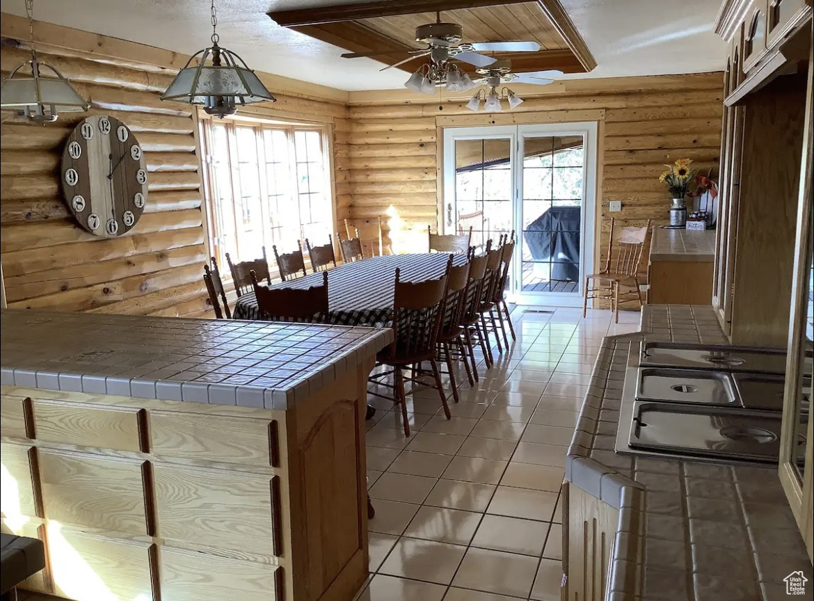 Dining space featuring rustic walls, ceiling fan, and light tile patterned floors