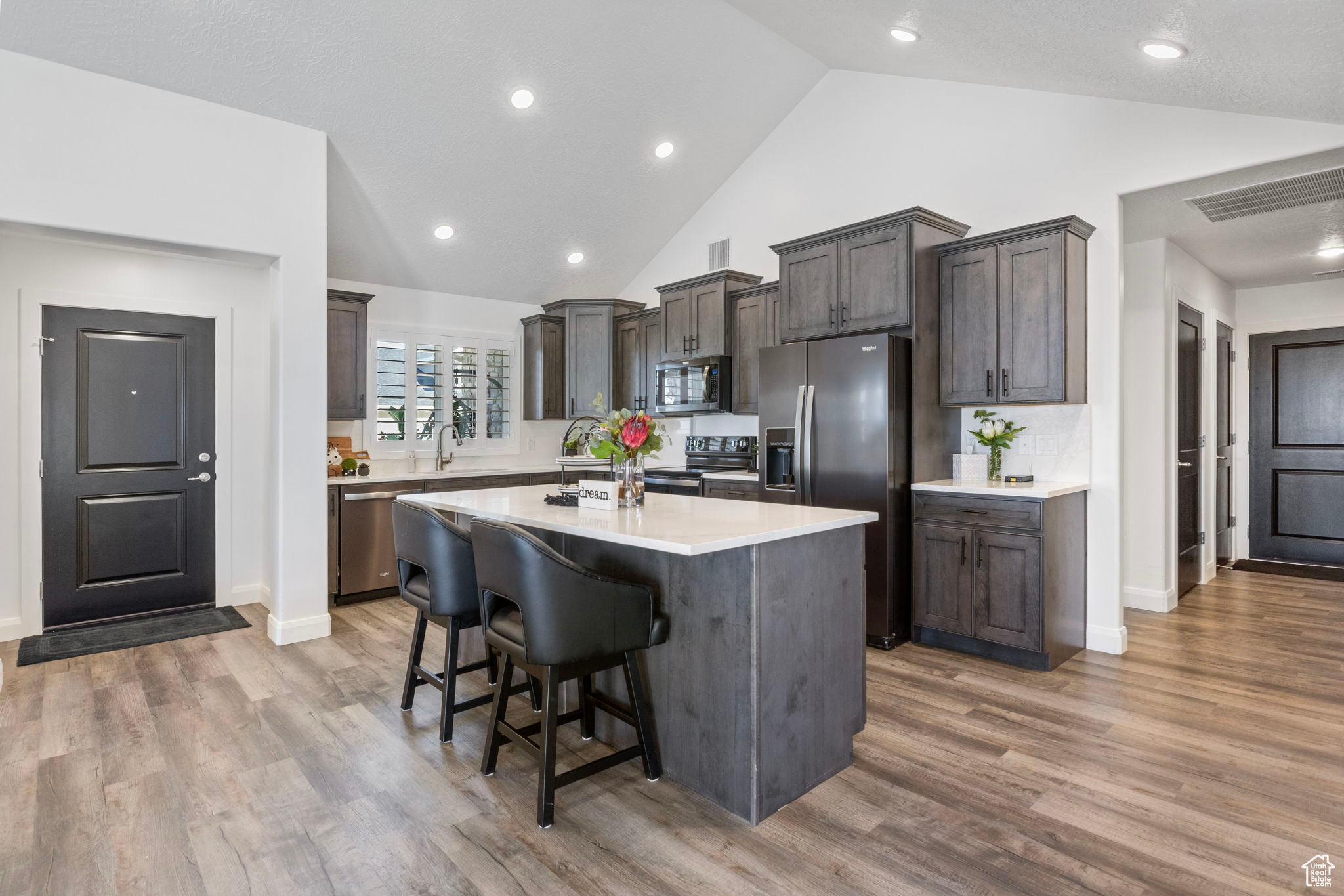 Kitchen with backsplash, a breakfast bar area, a kitchen island with sink, appliances with stainless steel finishes, and hardwood / wood-style flooring
