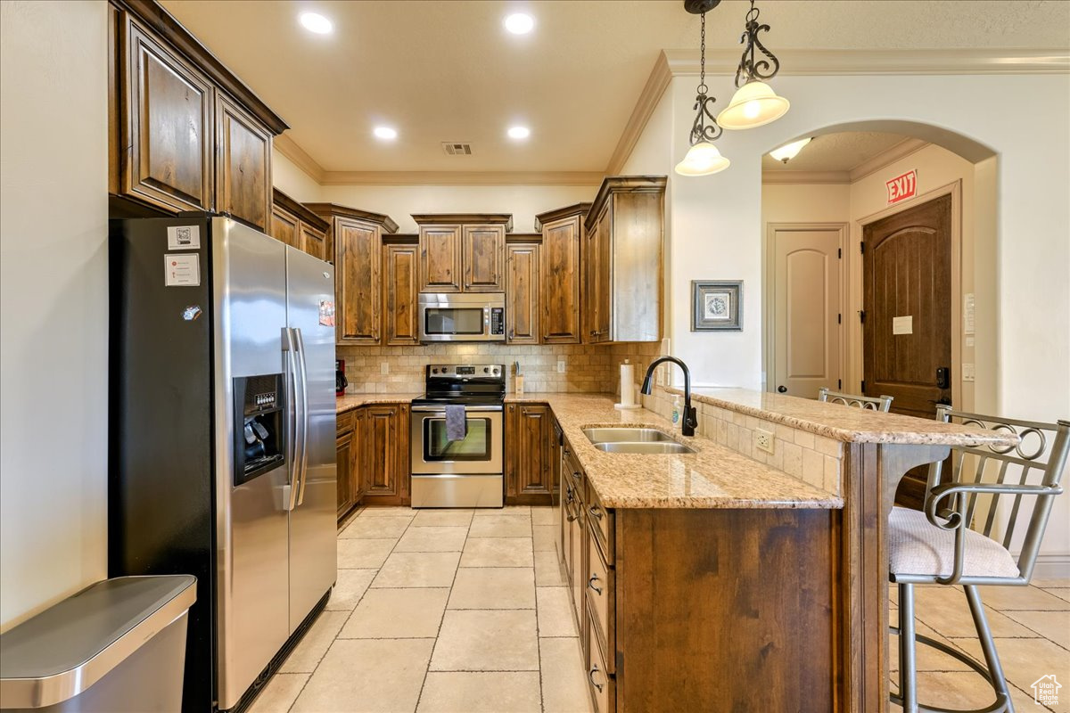 Kitchen featuring sink, hanging light fixtures, stainless steel appliances, a kitchen bar, and light tile patterned floors