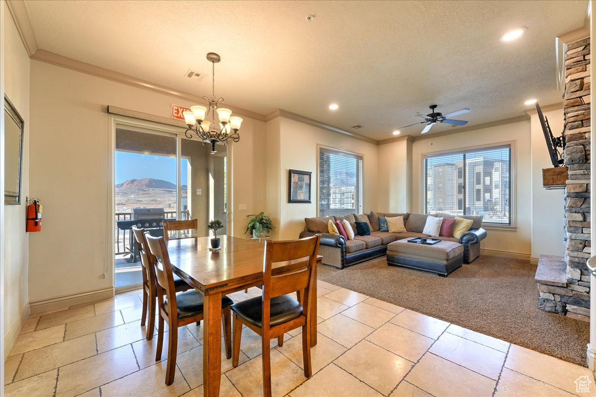 Dining space featuring a mountain view, a stone fireplace, ornamental molding, and ceiling fan with notable chandelier