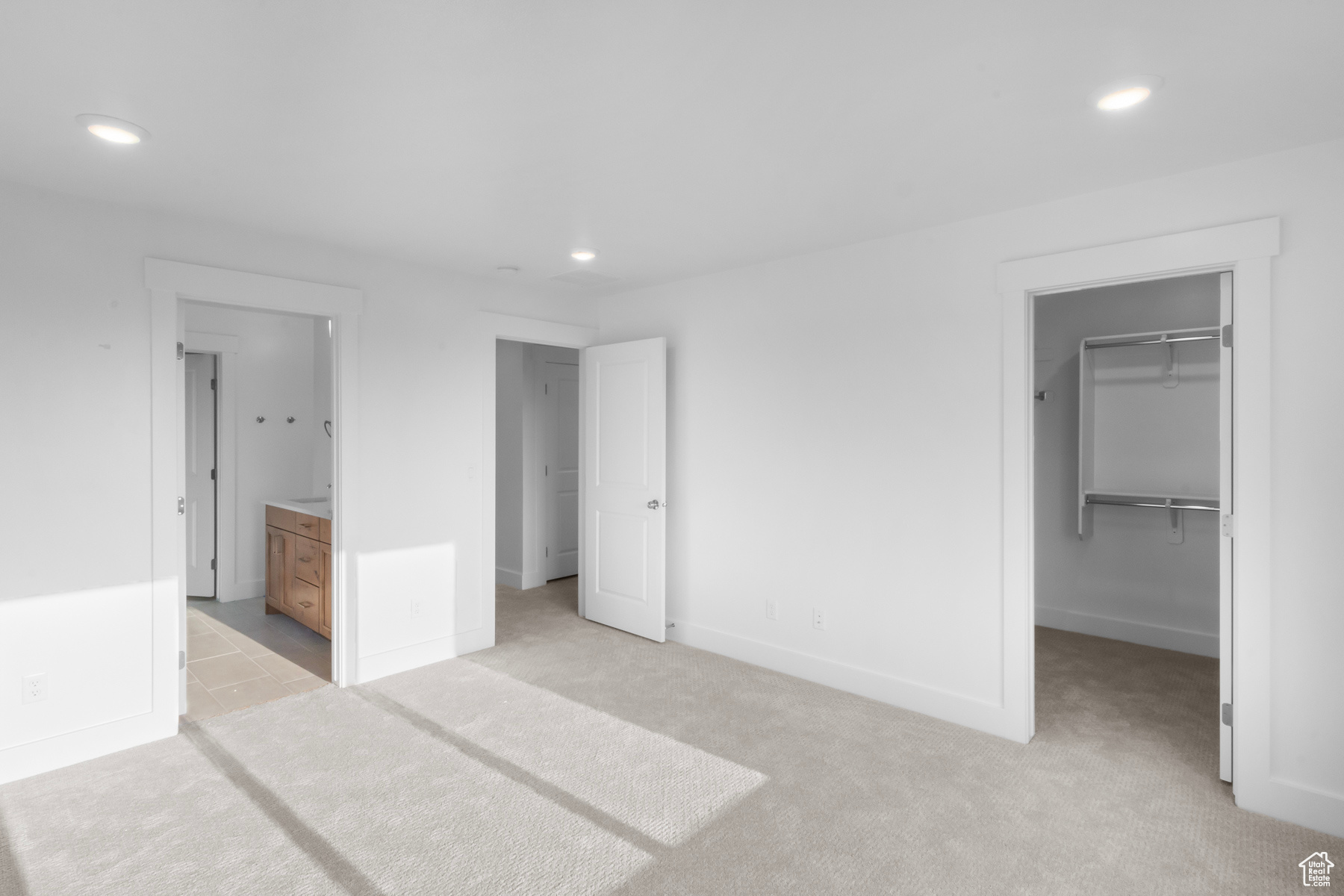 Unfurnished bedroom with light carpet, a walk in closet, ensuite bathroom, and a closet