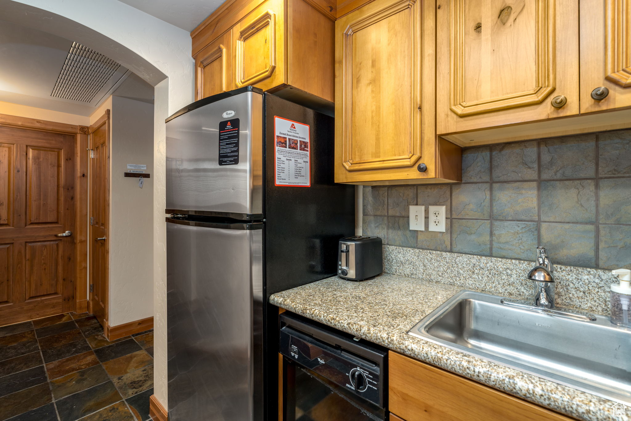 Kitchen featuring dishwasher, sink, tasteful backsplash, light stone counters, and stainless steel fridge