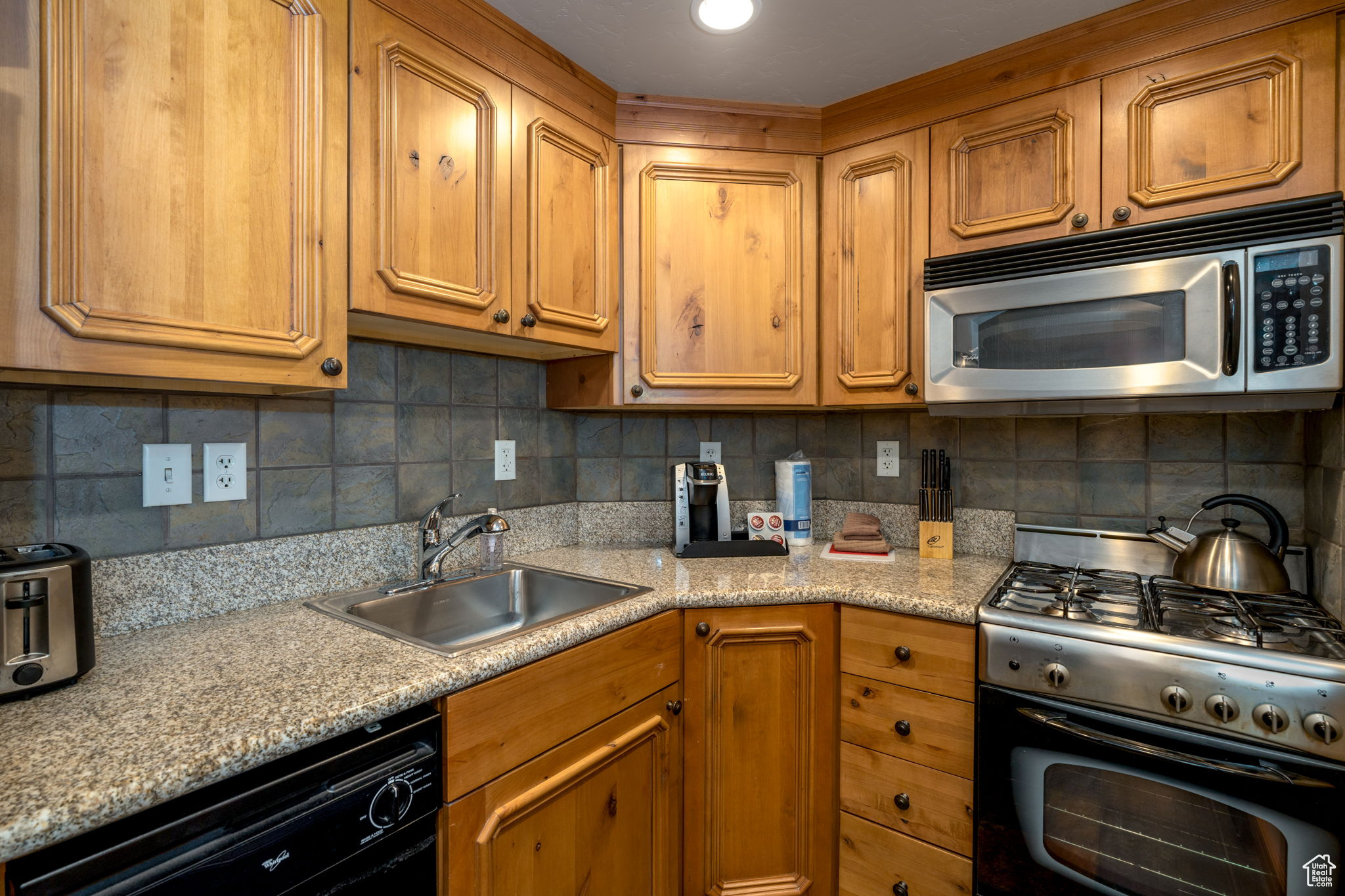 Kitchen with backsplash, light stone counters, sink, and stainless steel appliances