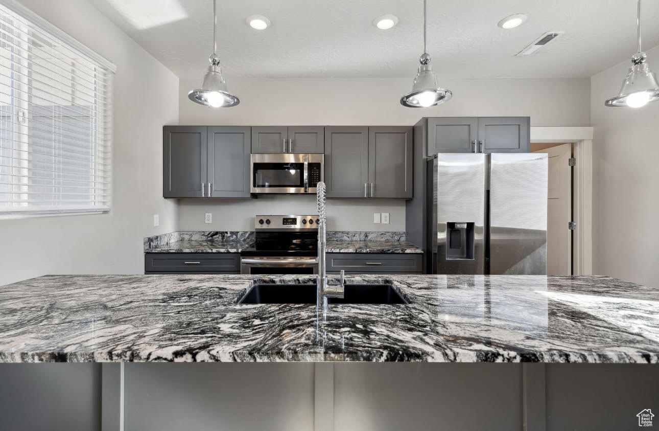 Kitchen featuring pendant lighting, gray cabinets, stone counters, and appliances with stainless steel finishes