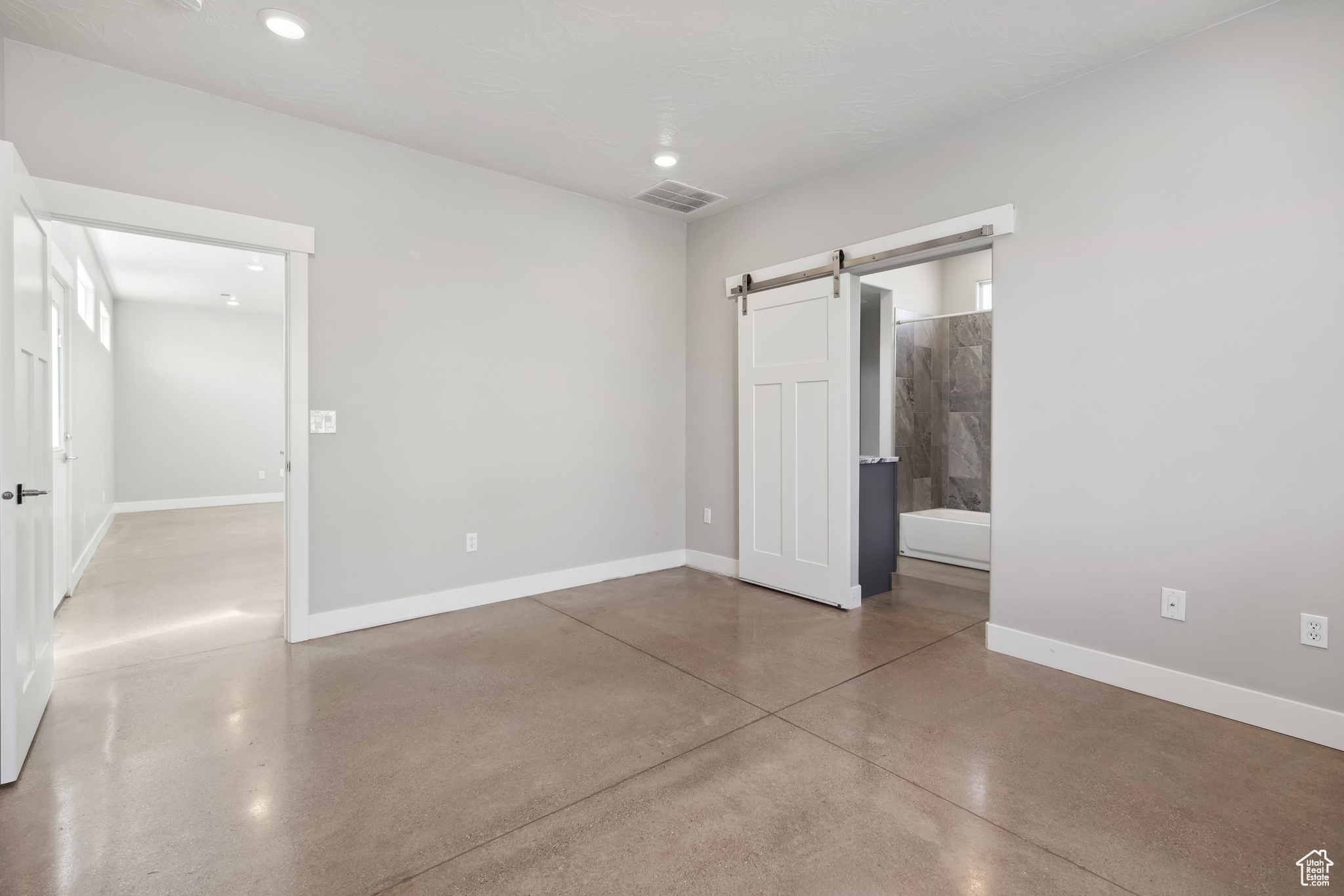 Unfurnished bedroom featuring concrete flooring, a barn door, and ensuite bathroom