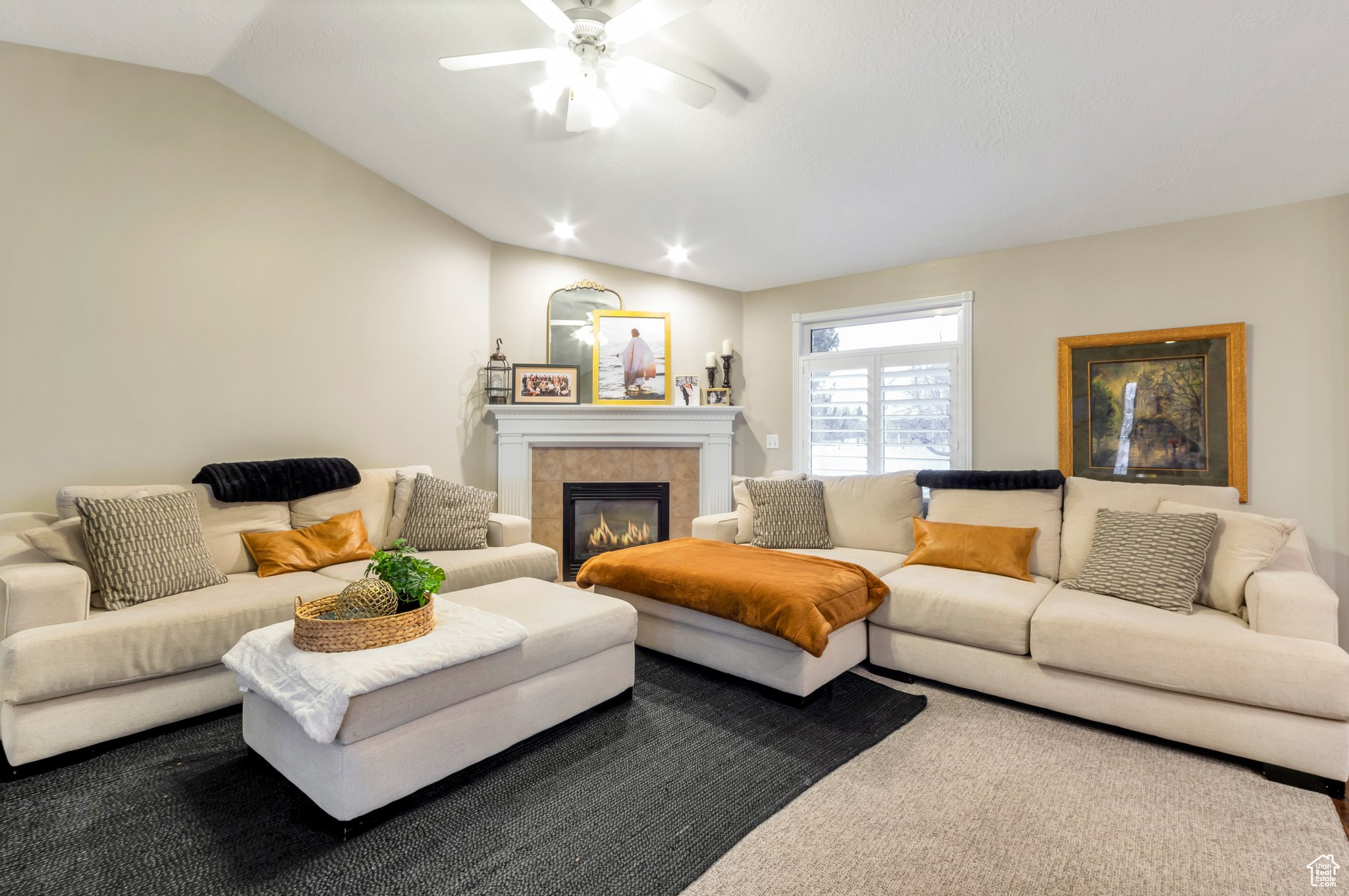 Carpeted living room with a tiled fireplace, ceiling fan, and lofted ceiling