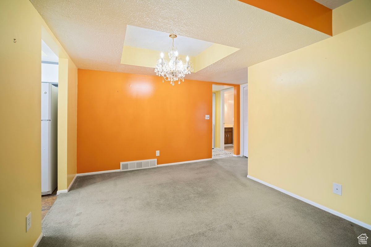 Spare room with a textured ceiling, a raised ceiling, a chandelier, and carpet flooring