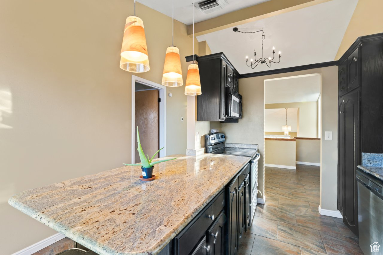 Kitchen with stainless steel appliances, decorative light fixtures, an inviting chandelier, and light stone countertops