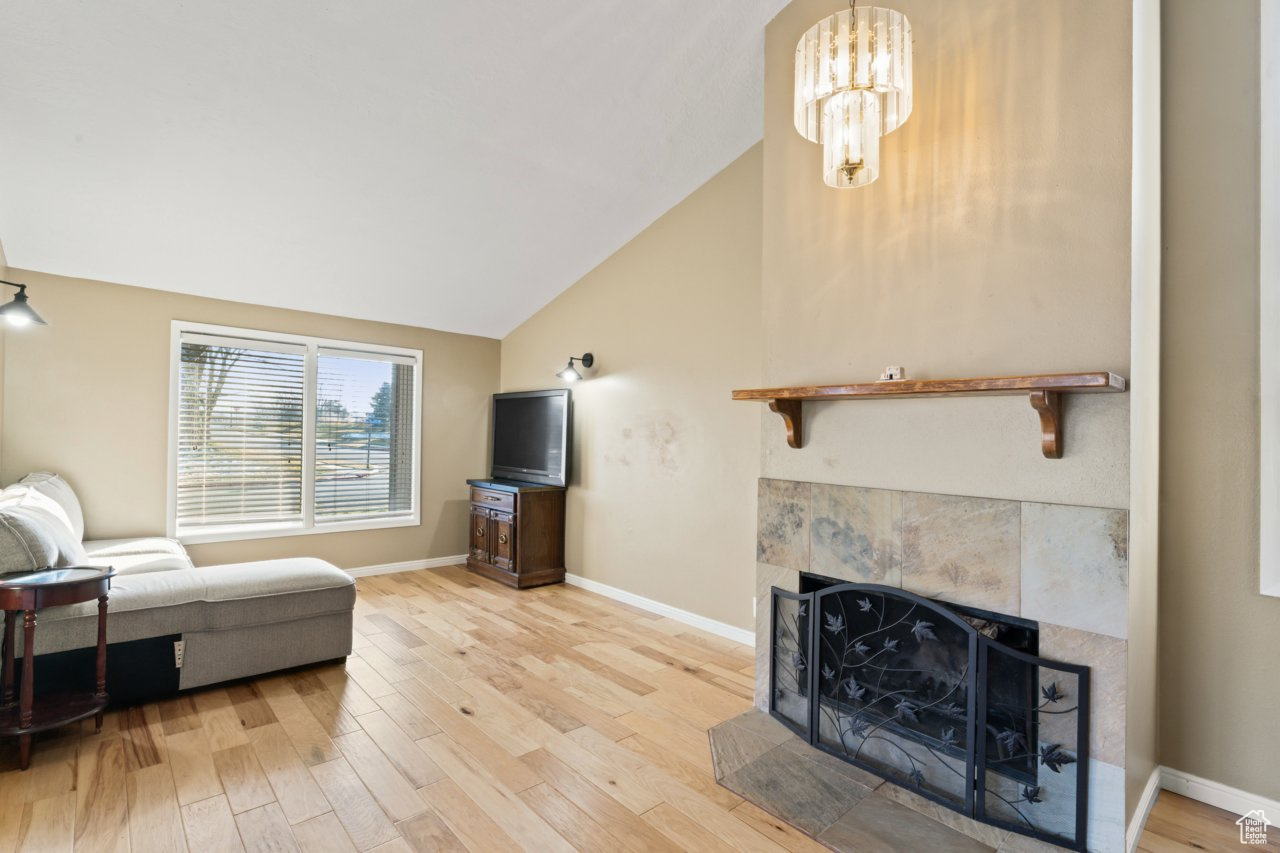 Living room with light wood-type flooring, a chandelier, vaulted ceiling, and a fireplace