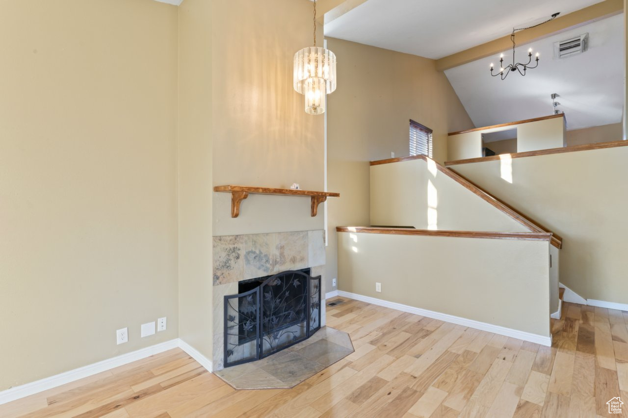 Unfurnished living room featuring lofted ceiling with beams, a fireplace, a chandelier, and light hardwood / wood-style flooring