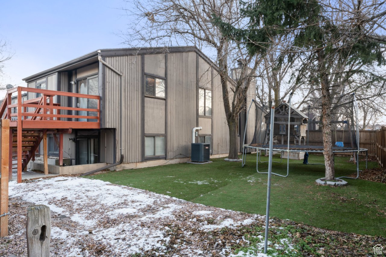 Snow covered property featuring a deck, a yard, a trampoline, and central AC