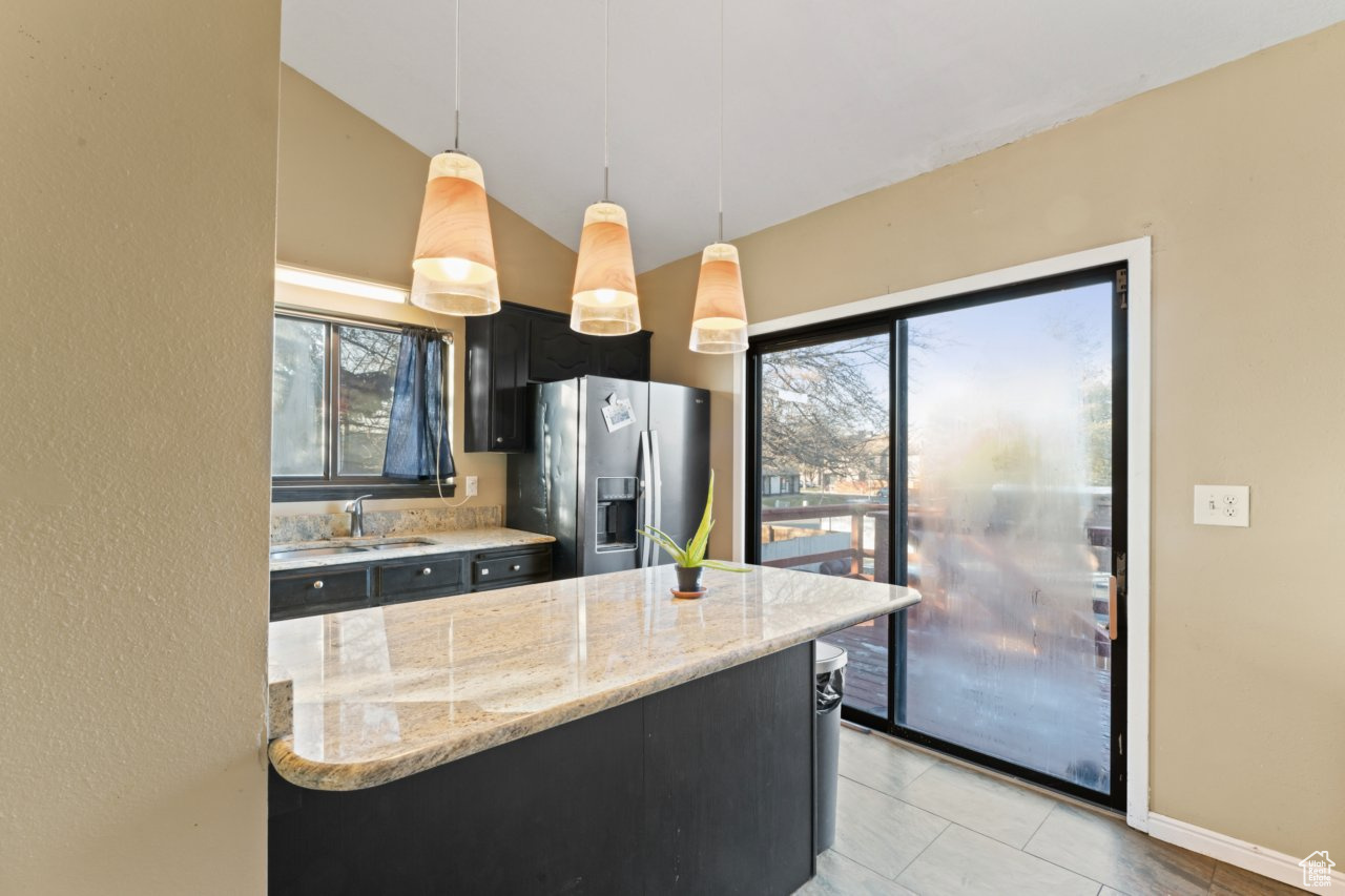 Kitchen featuring hanging light fixtures, light stone countertops, plenty of natural light, stainless steel refrigerator with ice dispenser, and lofted ceiling