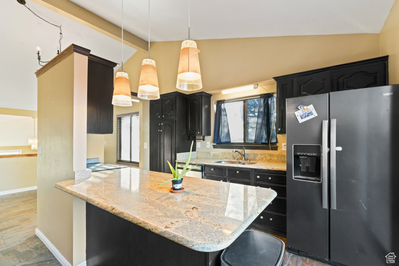 Kitchen with stainless steel appliances, sink, decorative light fixtures, vaulted ceiling with beams, and light stone counters