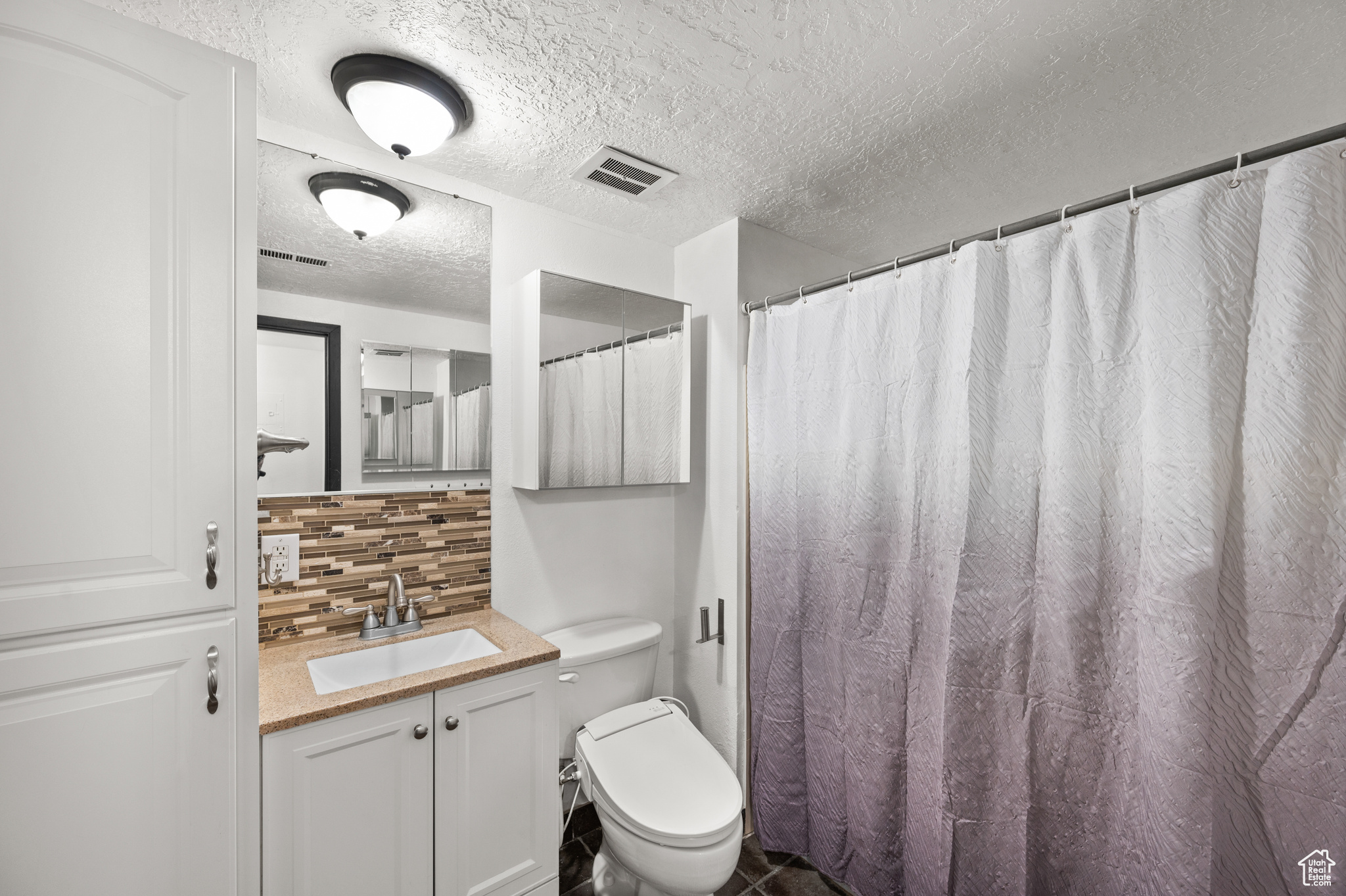 Bathroom with toilet, a textured ceiling, tub/shower, decorative backsplash, and vanity