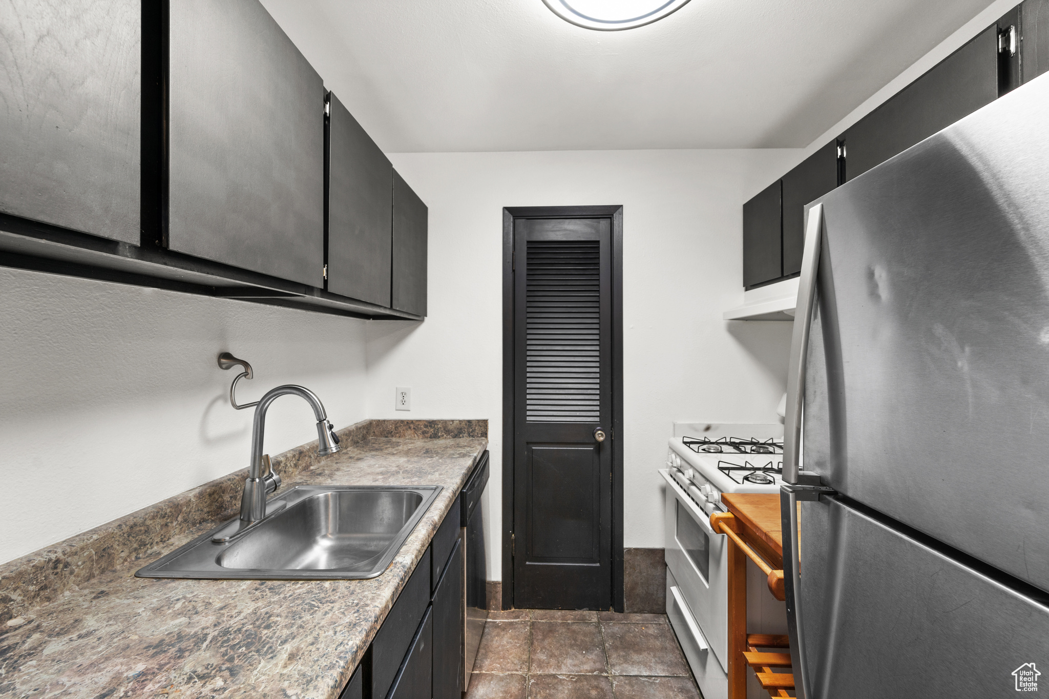 Kitchen with sink, white gas range oven, stainless steel refrigerator, and dishwashing machine