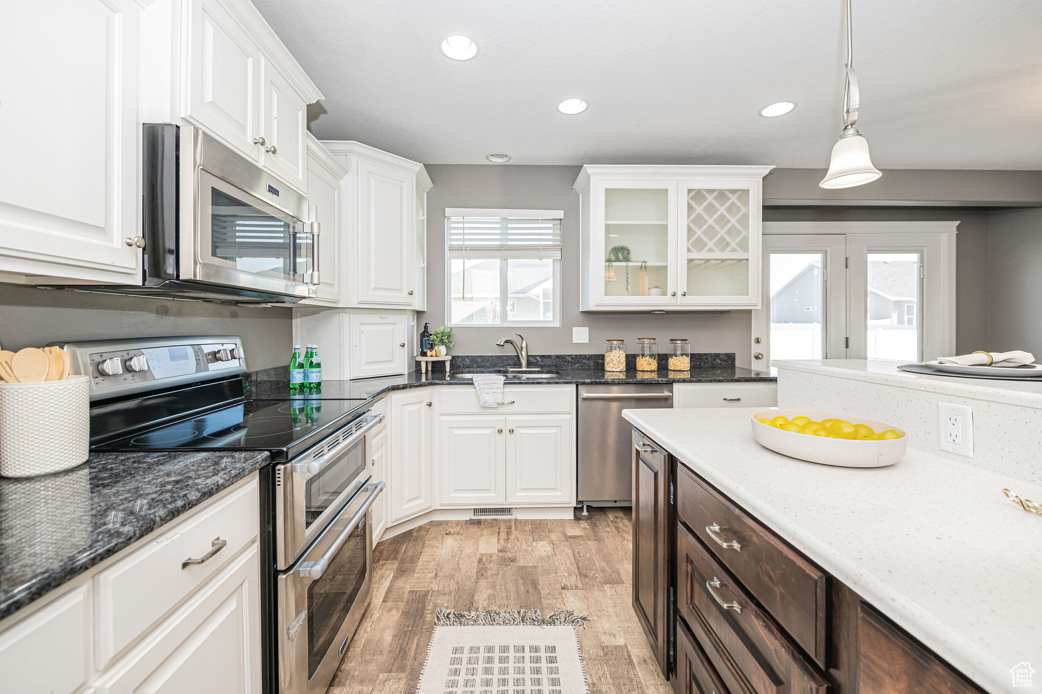 Kitchen featuring sink, white cabinetry, light hardwood / wood-style floors, hanging light fixtures, and appliances with stainless steel finishes