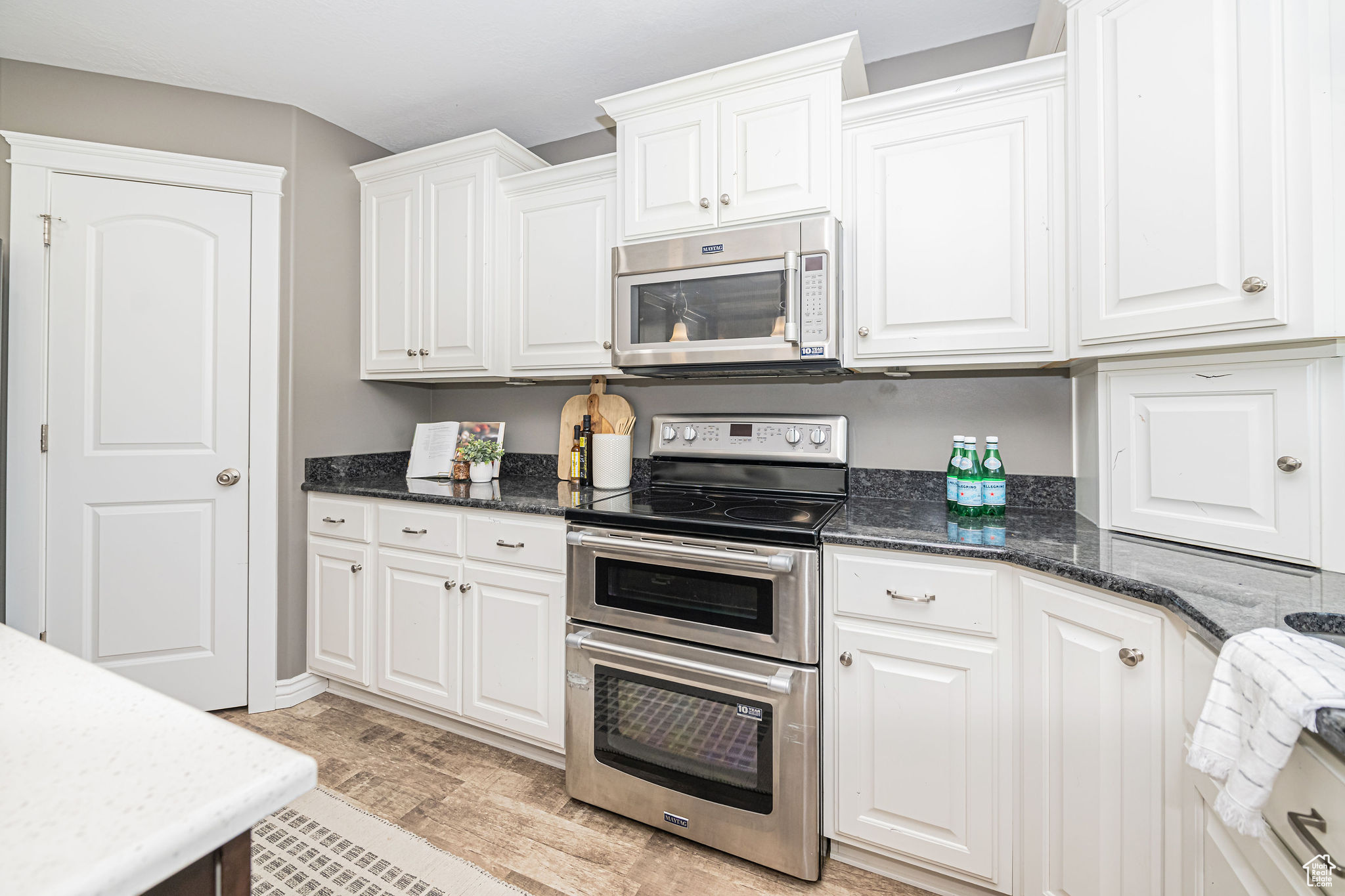 Kitchen with stainless steel appliances, white cabinets, light wood-type flooring, and dark stone counters