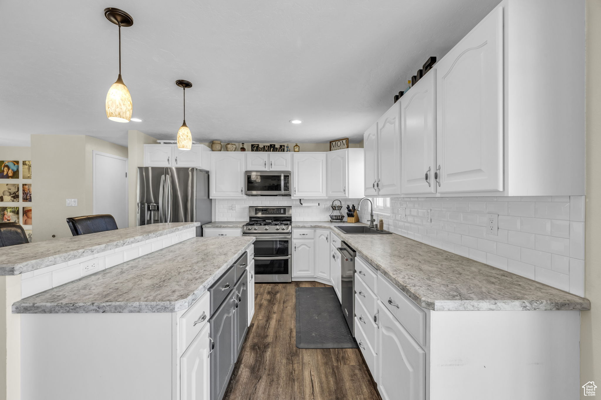 Kitchen featuring stainless steel appliances, white cabinets, pendant lighting, and sink