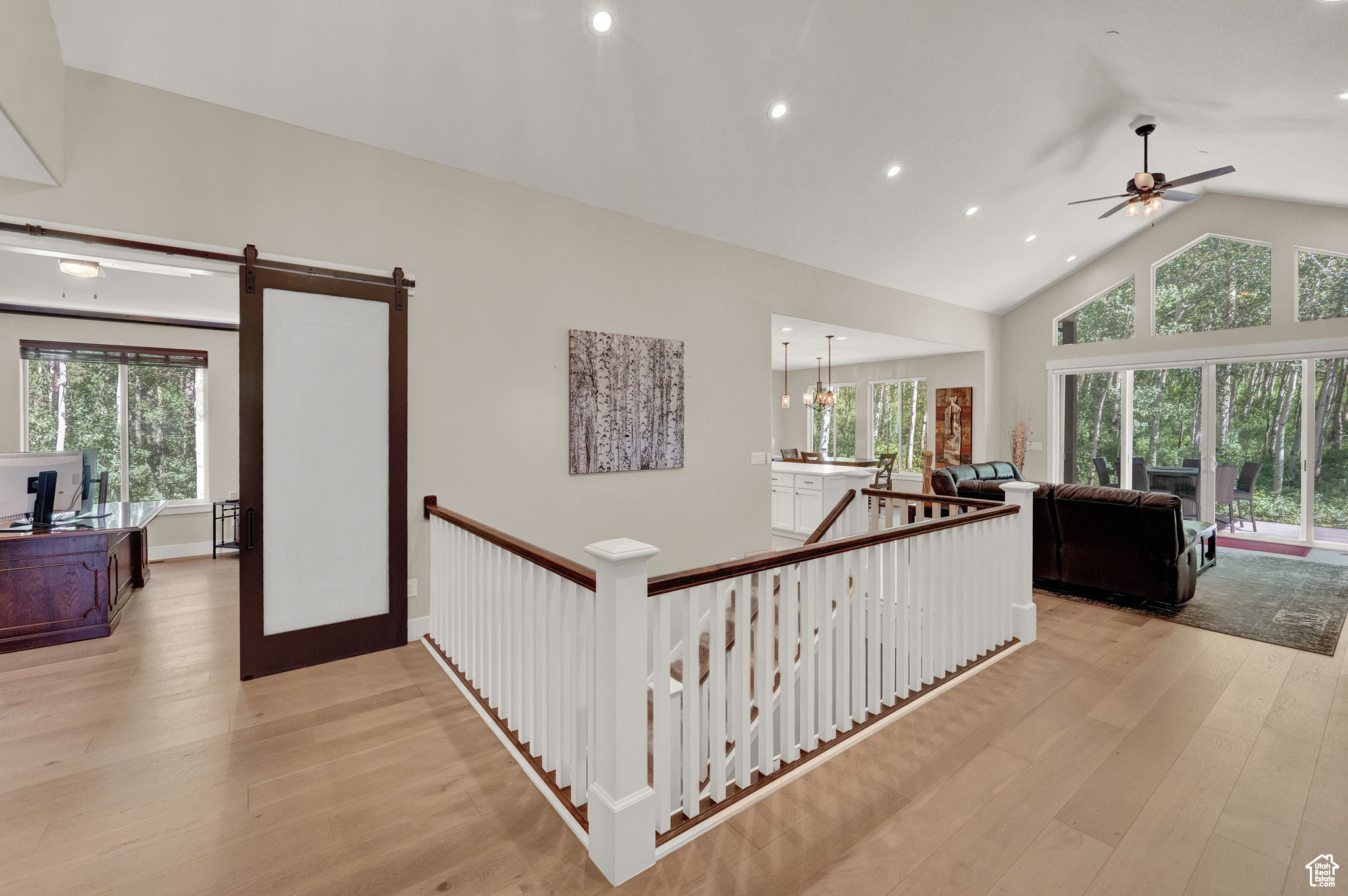 Hallway featuring a healthy amount of sunlight, light wood-type flooring, high vaulted ceiling, and a notable chandelier