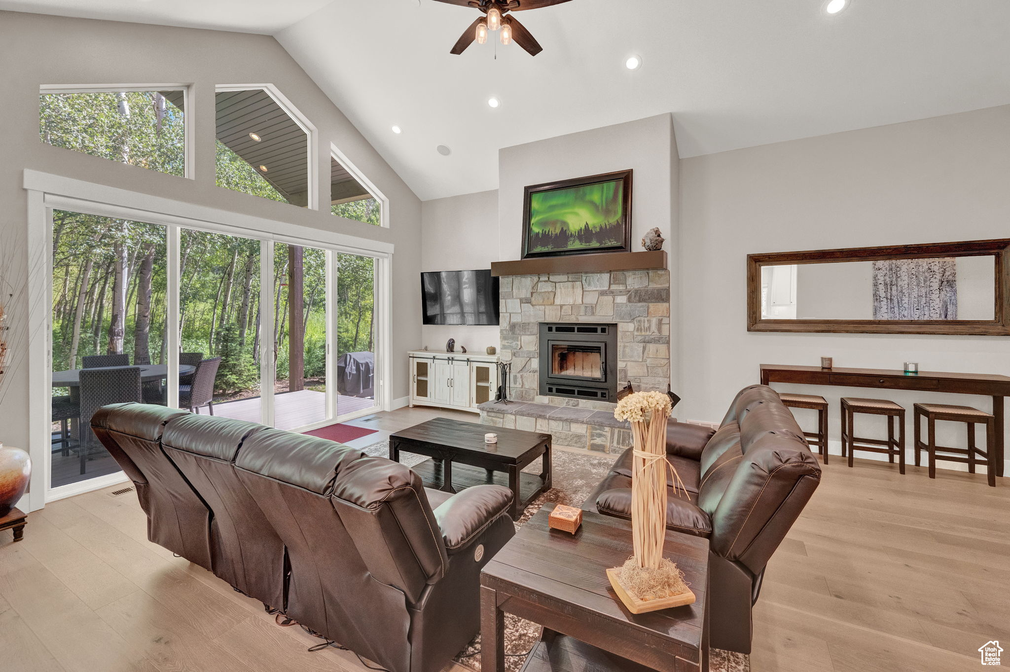 Living room with high vaulted ceiling, ceiling fan, light hardwood / wood-style floors, and a stone fireplace