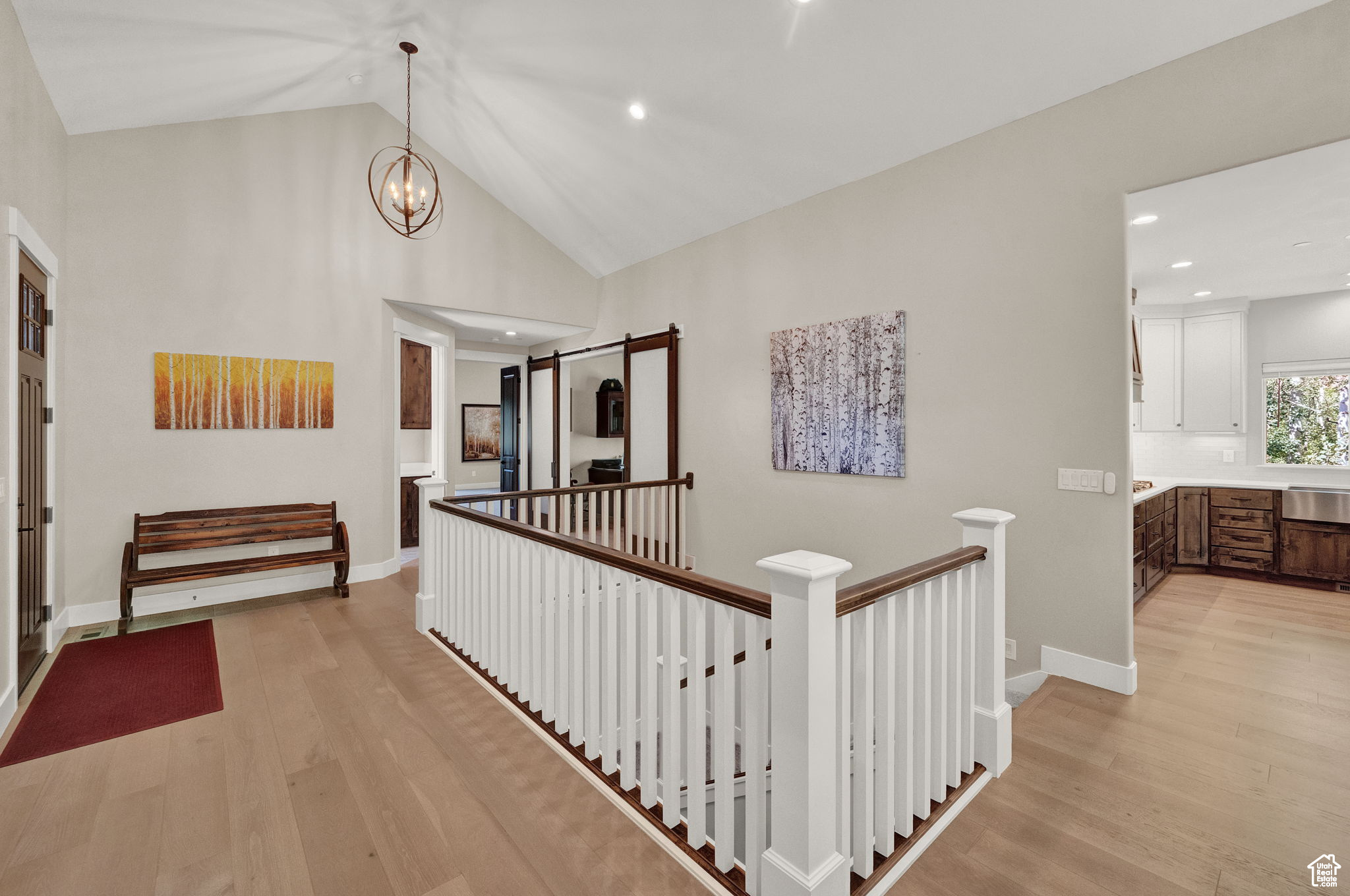 Hall with high vaulted ceiling, an inviting chandelier, and light wood-type flooring