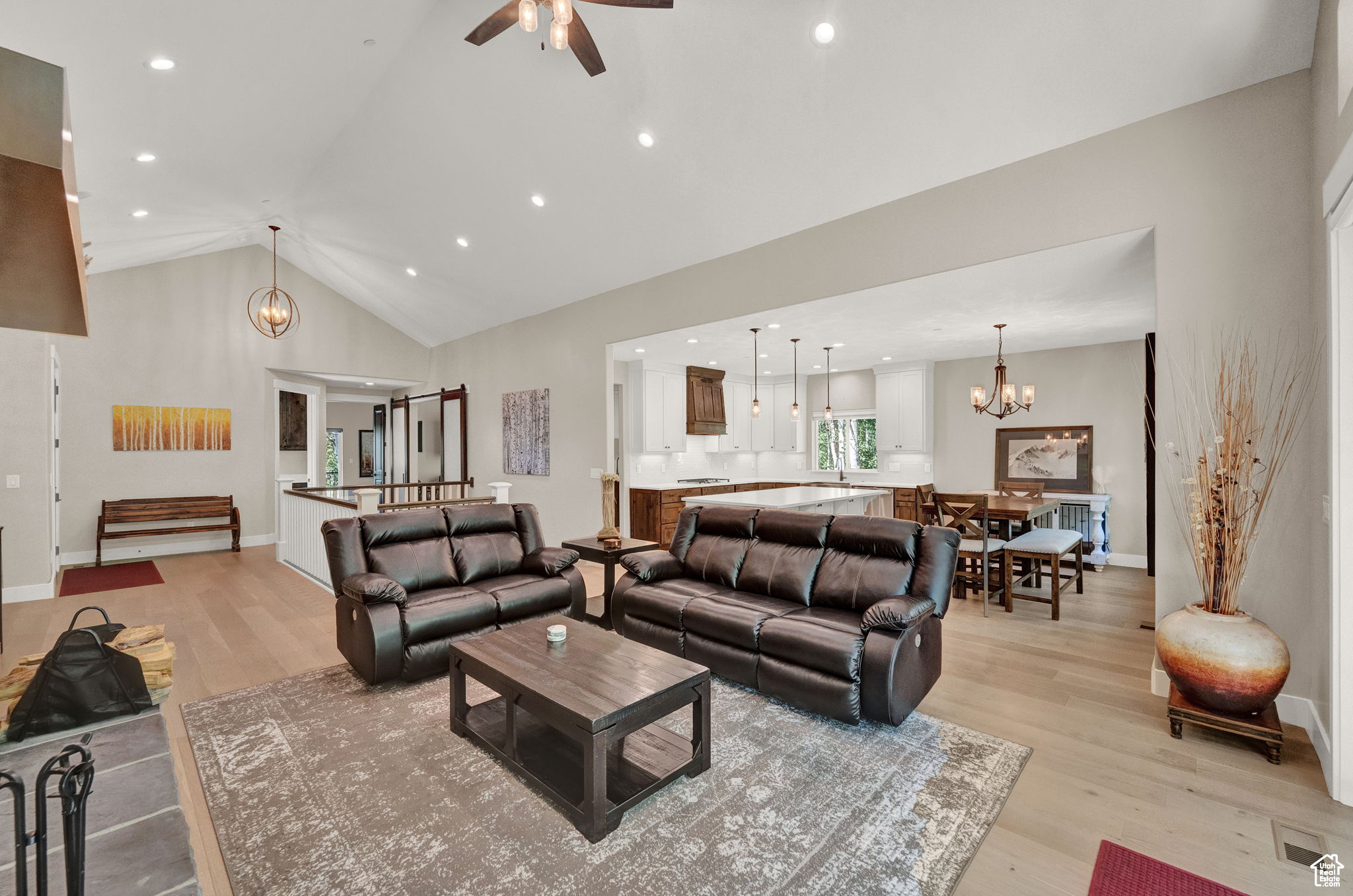 Living room with ceiling fan with notable chandelier, high vaulted ceiling, and light hardwood / wood-style flooring