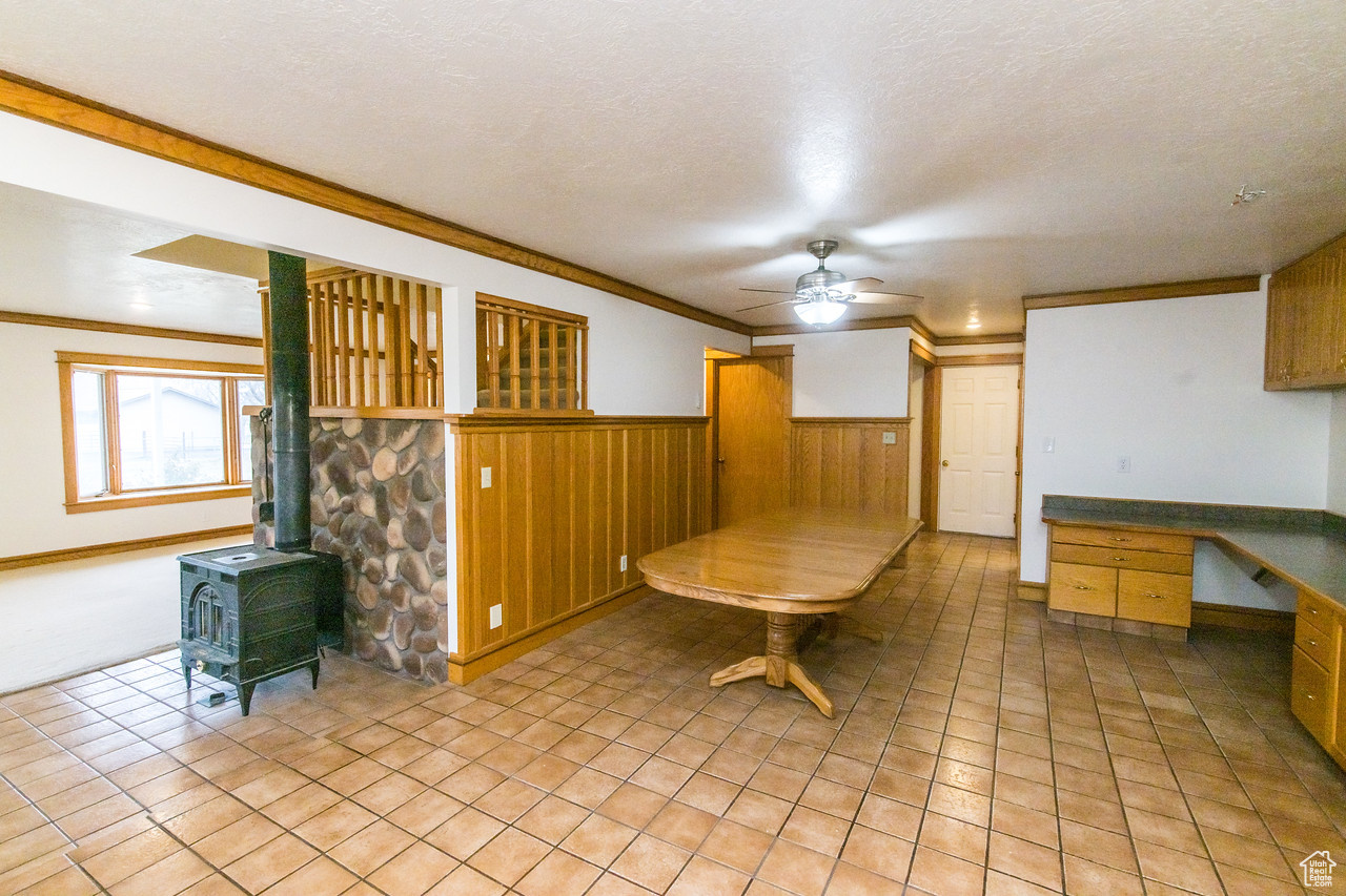 Tiled dining room with built in desk, a wood stove, ceiling fan, and oak details.