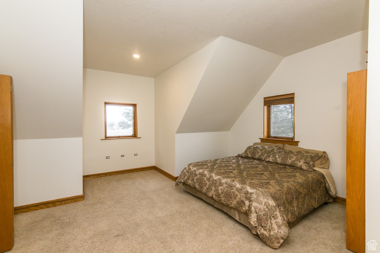 Bedroom with light colored carpet, vaulted ceiling, and multiple windows