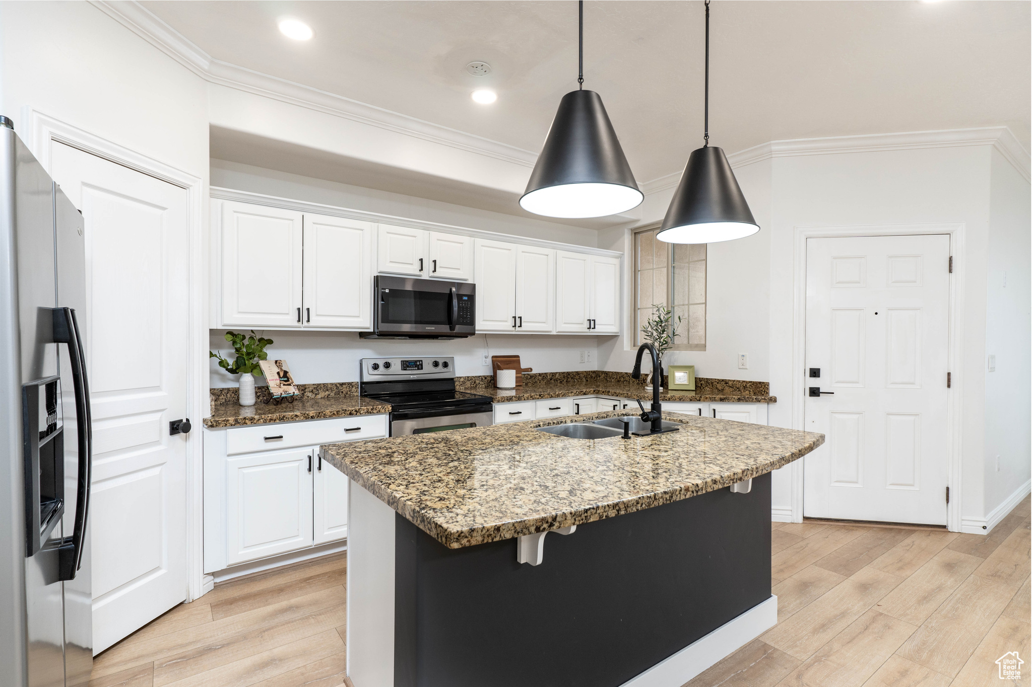 Kitchen featuring appliances with stainless steel finishes, an island with sink, pendant lighting, sink, and white cabinetry