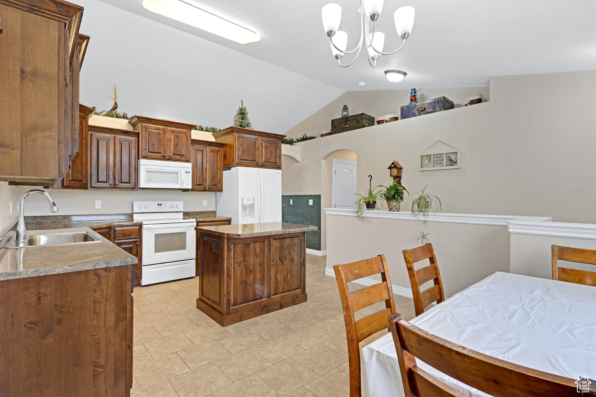 Kitchen with white appliances, a center island, decorative light fixtures, an inviting chandelier, and sink